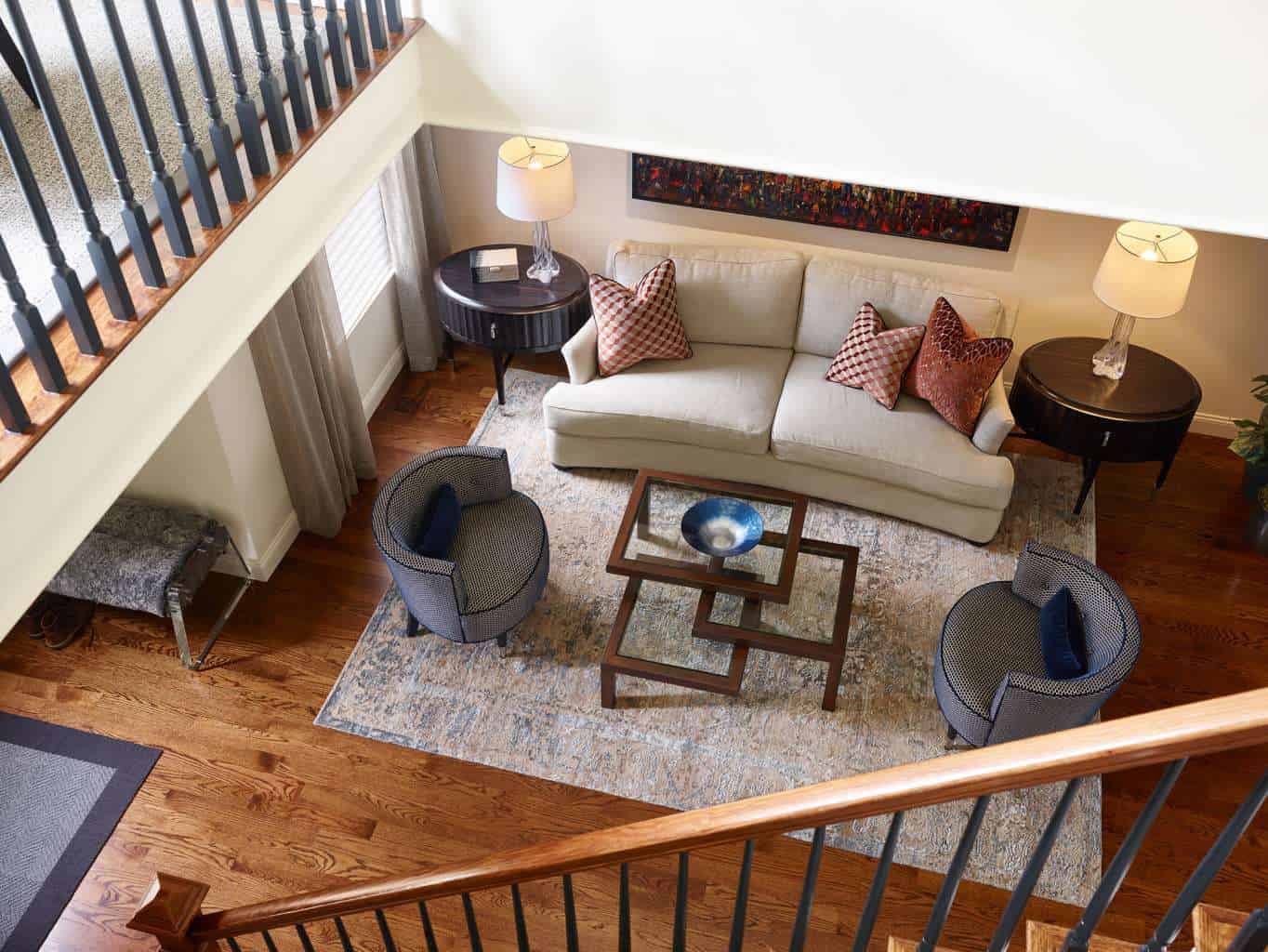A living room seen from above features a beige sofa, two blue chairs, a geometric glass coffee table, and decorative touches that reflect luxury interior design on wooden flooring—perfect inspiration from an interior designer Massachusetts.