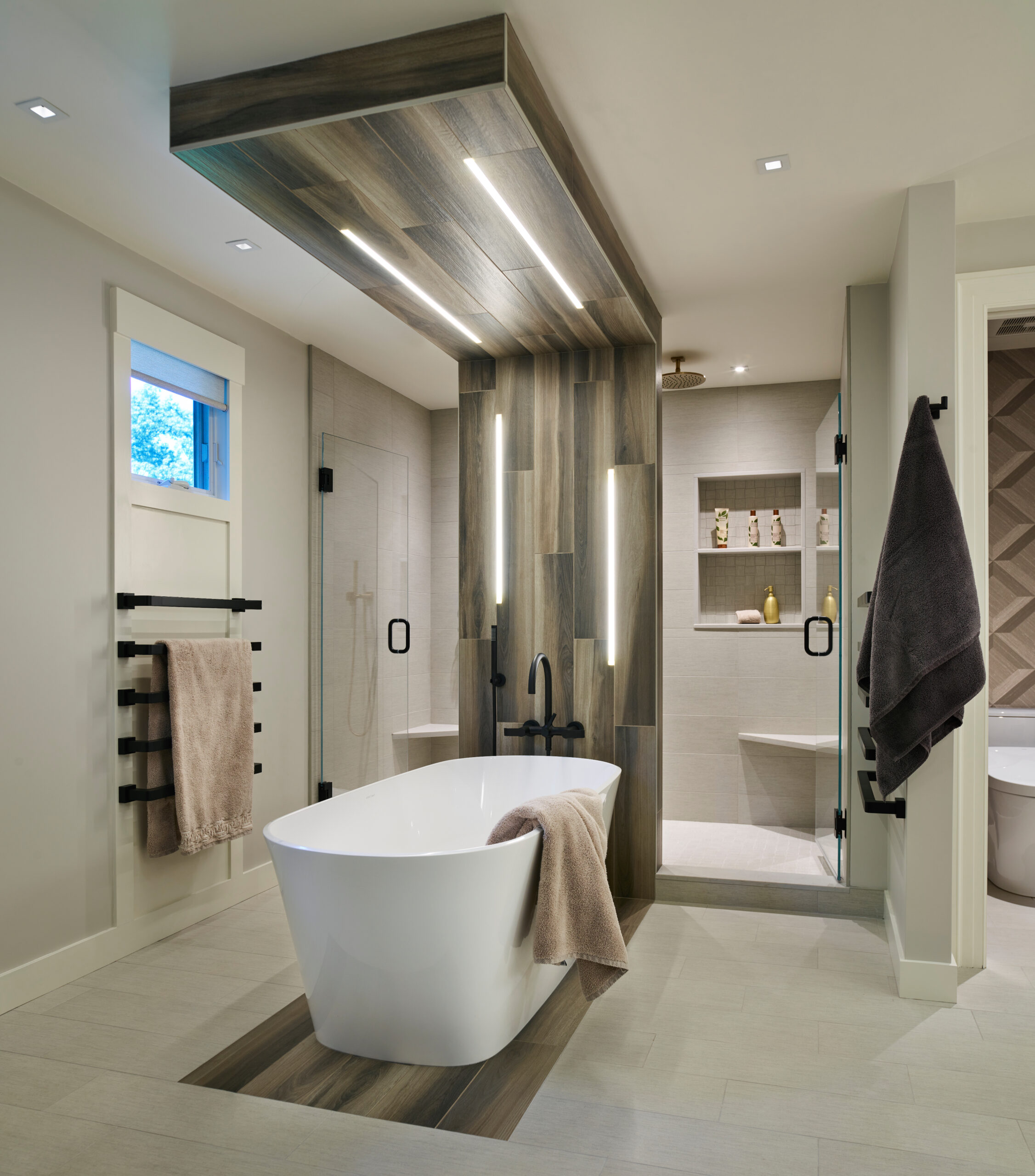 Modern bathroom with freestanding tub, wood-accented wall and ceiling, walk-in shower, towel racks, and neutral-toned tiles—an elegant example of Luxury Interior Design by a top Interior Designer Massachusetts.
