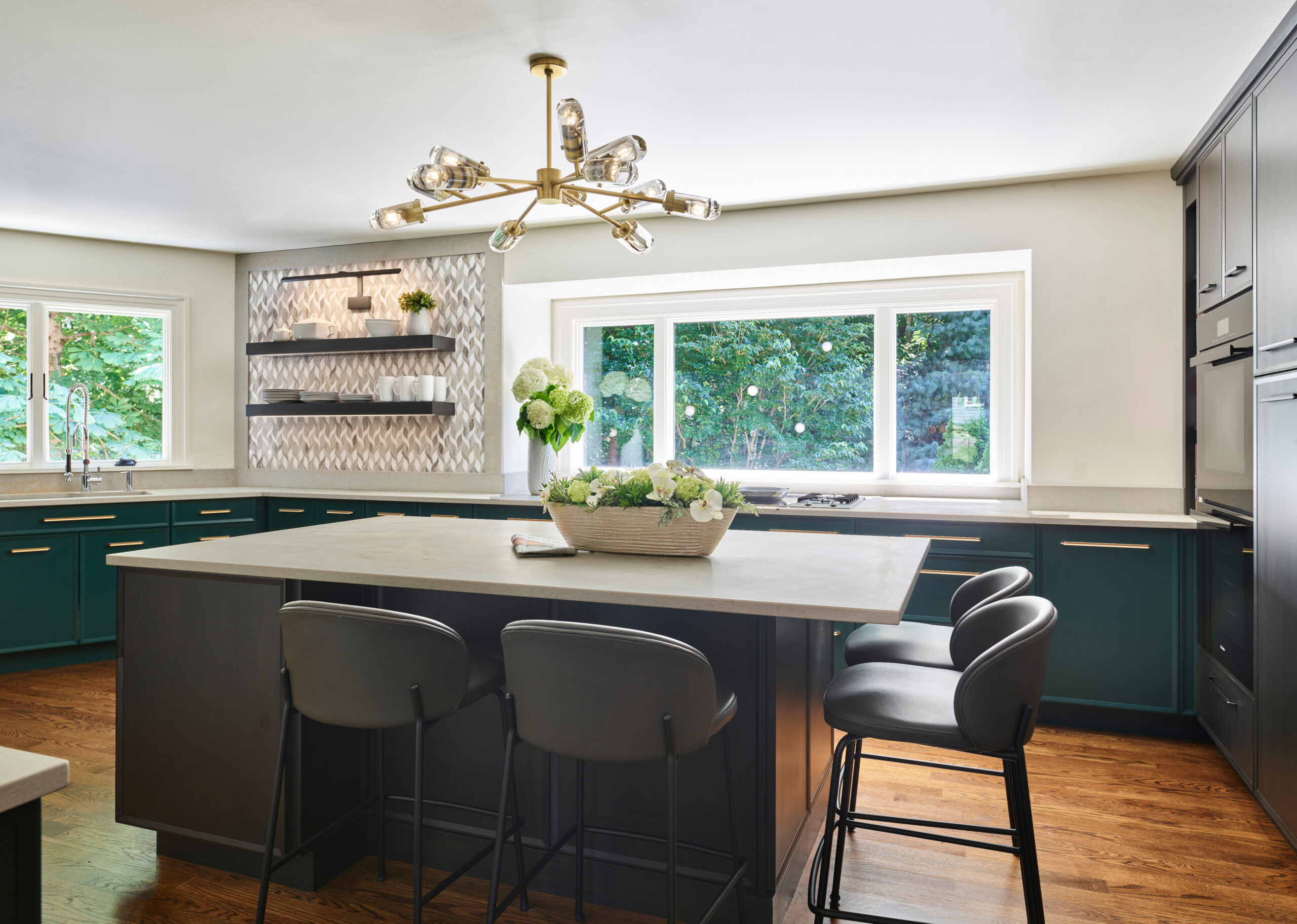 Modern kitchen with green cabinets, a large island with gray barstools, geometric backsplash, and a gold chandelier. Designed by an Interior Designer in Massachusetts, this space blends contemporary style with luxury interior design elements.