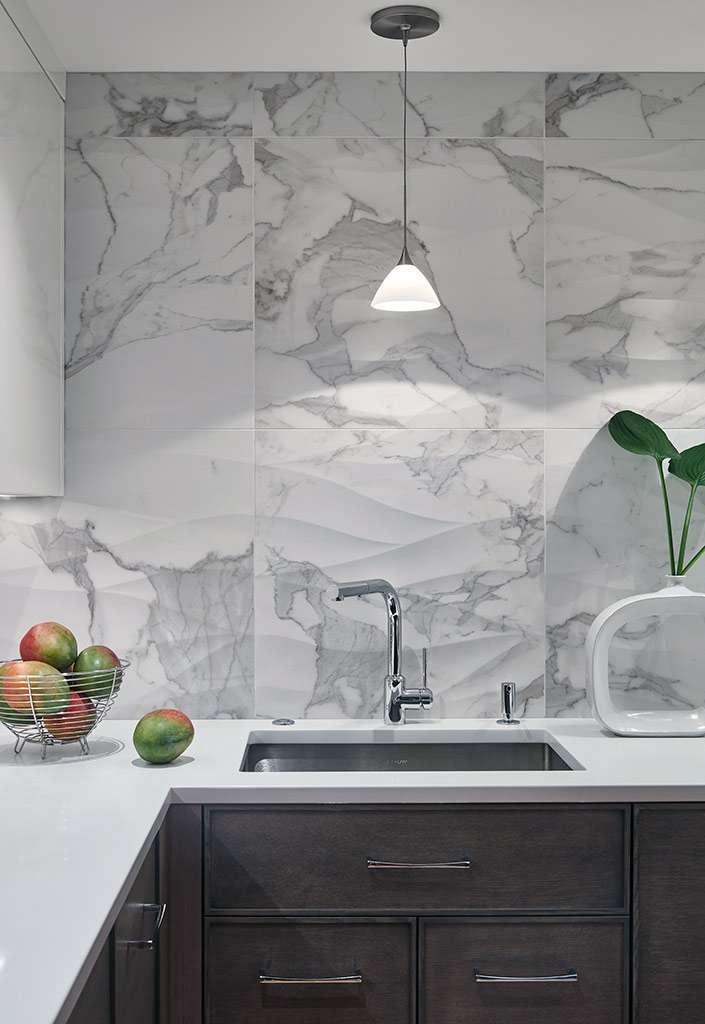 Modern kitchen with a marble backsplash, single pendant light, dark wood cabinetry, and stainless steel sink—an elegant example of Luxury Interior Design by an expert Interior Designer Massachusetts. Vase and bowl of apples add a fresh touch.