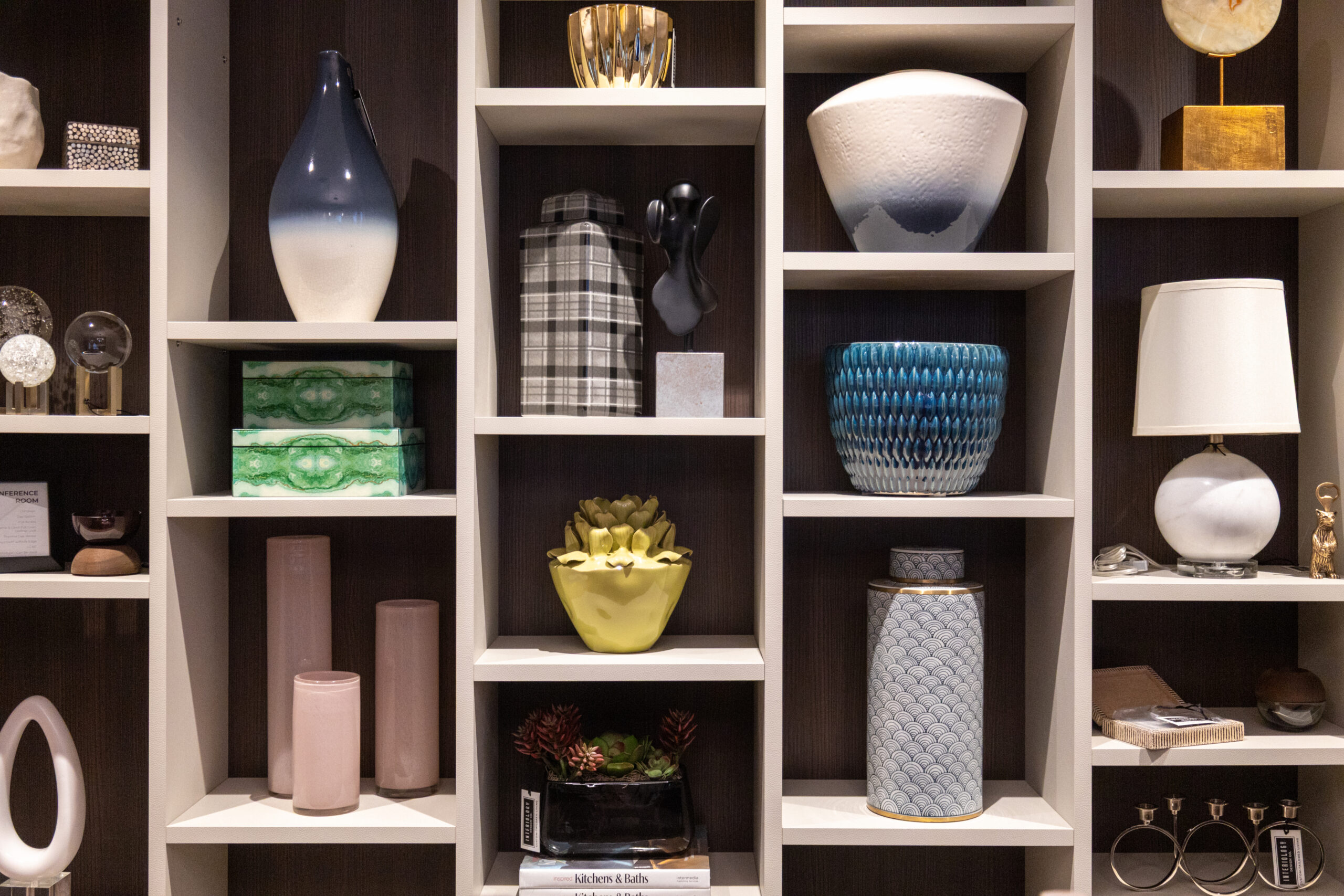 A shelving unit by a luxury interior design expert displays various decorative objects including vases, boxes, lamps, and plants arranged neatly in individual compartments.