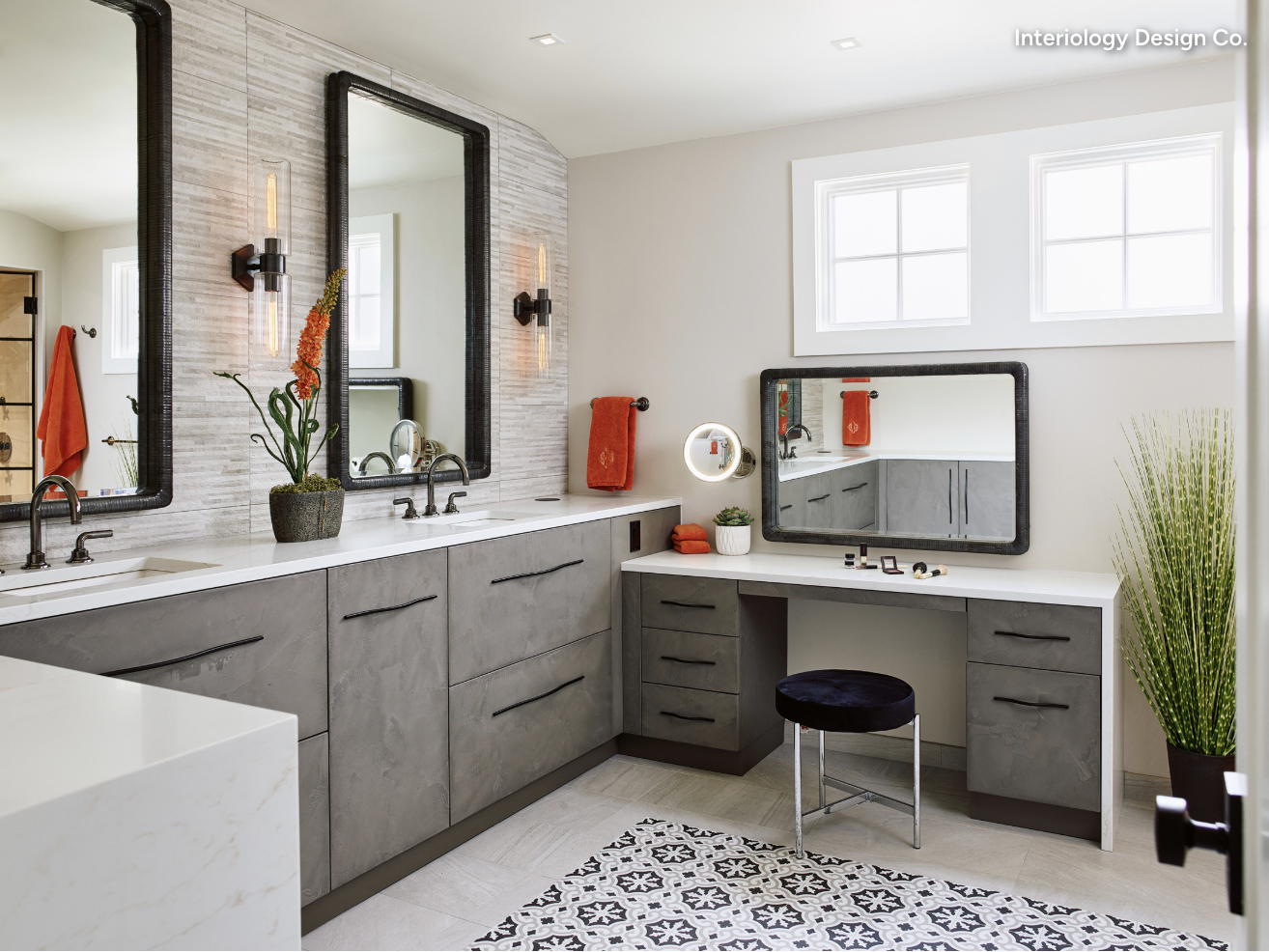 Modern bathroom with dual sinks, large mirrors, a makeup vanity with a round stool, decorative plants, and patterned floor tile. Bright lighting from windows and wall sconces reflects true luxury interior design.