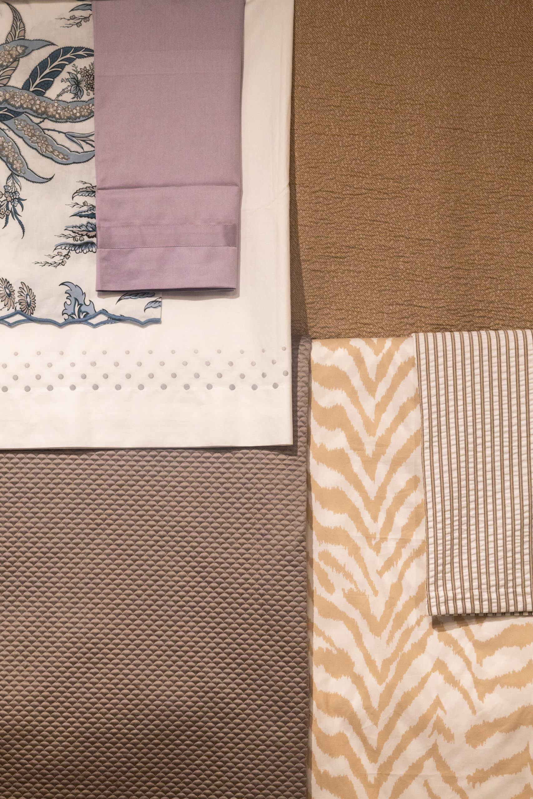 Several folded fabrics are arranged side by side, featuring stripes, animal print, dots, and a floral design in neutral and pastel tones—perfect accents for a luxury interior design scheme curated by an expert interior designer in Massachusetts.