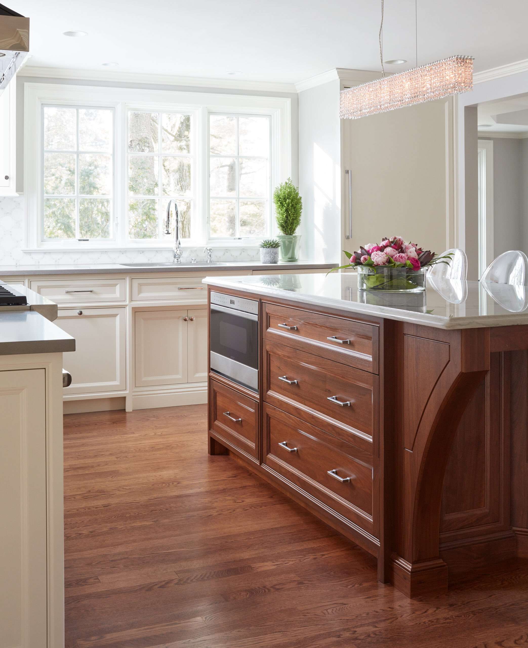 A modern kitchen with a wooden island, built-in microwave, white cabinets, large windows, and a flower arrangement on the counter—showcasing luxury interior design by an expert interior designer in Massachusetts.