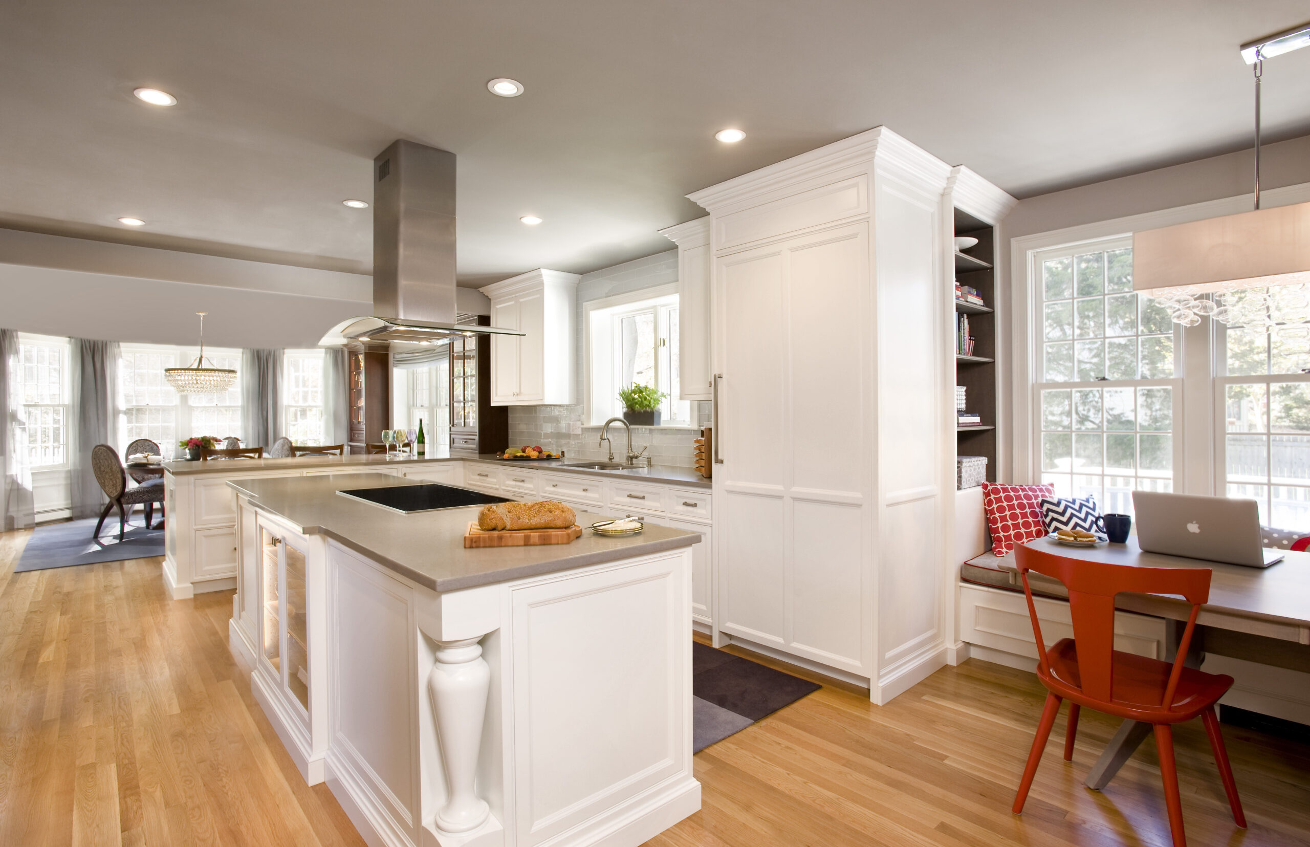 Modern kitchen with white cabinets, gray countertops, a central island cooktop, and a built-in breakfast nook—expertly crafted by an Interior Designer Massachusetts—for a touch of luxury interior design and comfort by large windows.