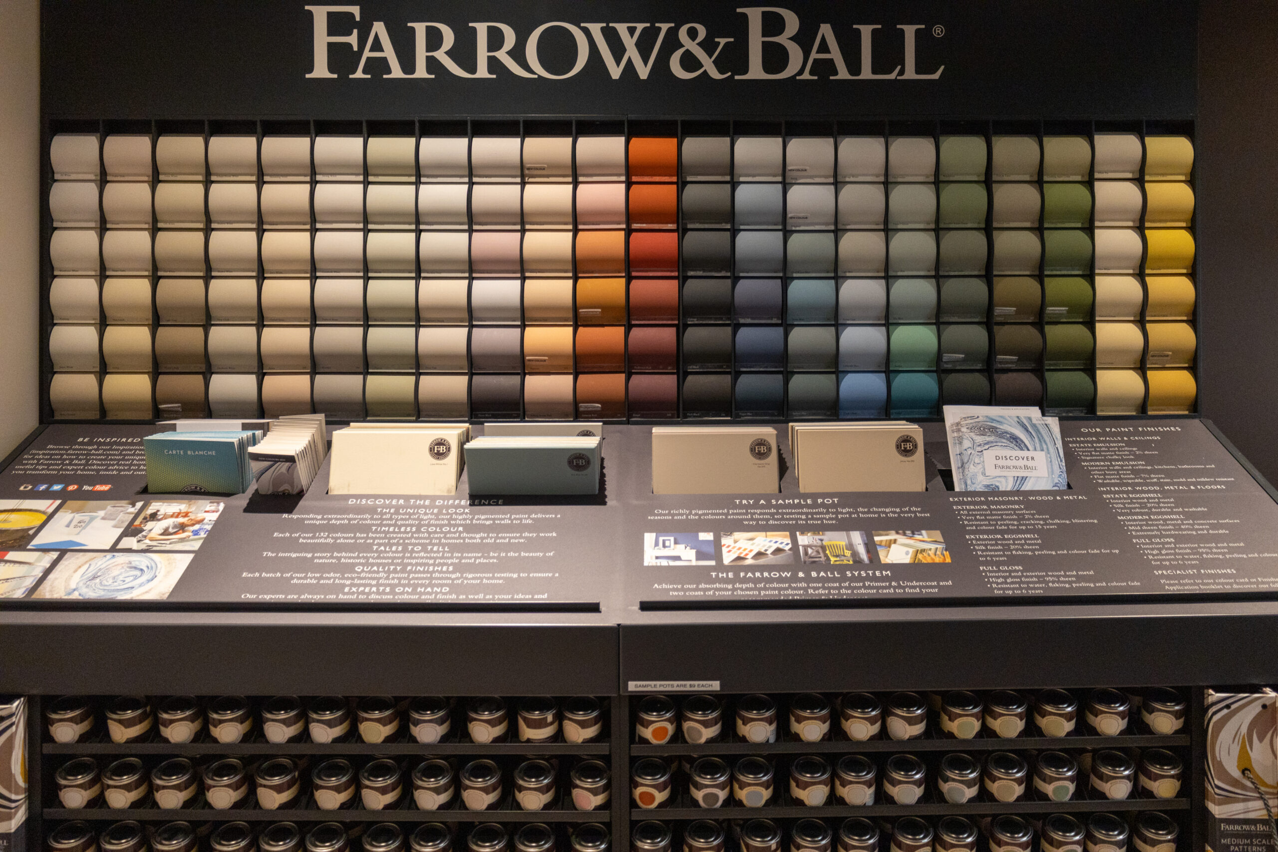 Display of Farrow & Ball paint sample cards arranged by color, with sample pots and informational panels below—a perfect inspiration source for anyone interested in luxury interior design or working with an interior designer in Massachusetts.