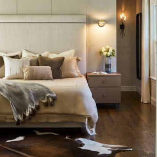 Modern bedroom with a beige bed, multiple pillows, a gray throw, and cowhide rug on wooden floors—an inviting retreat crafted by a leading Interior Designer Massachusetts for those who appreciate luxury interior design.
