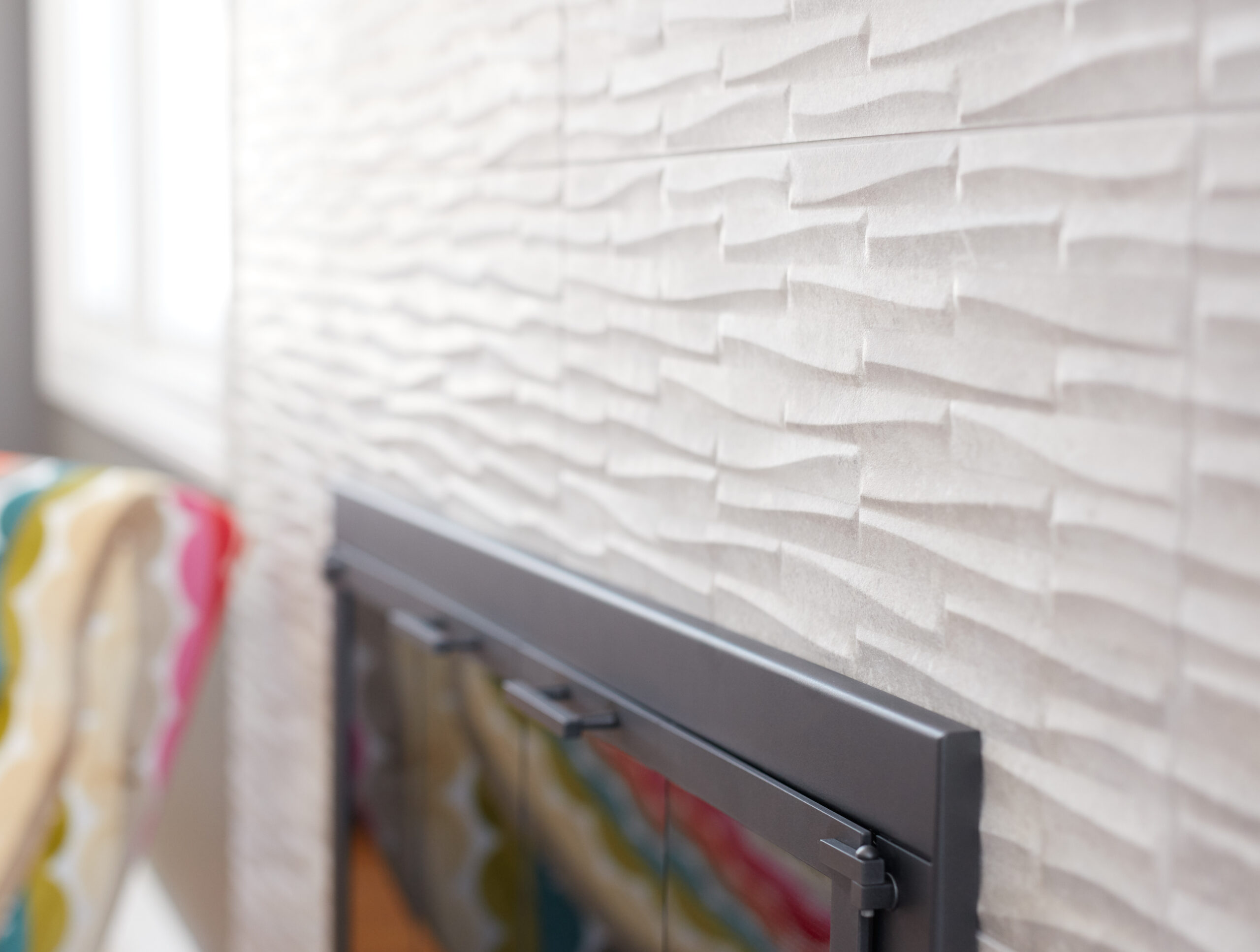 Textured white wall tiles above a black-framed fireplace, with a colorful striped fabric visible on the left side—showcasing luxury interior design as crafted by an expert Interior Designer Massachusetts.