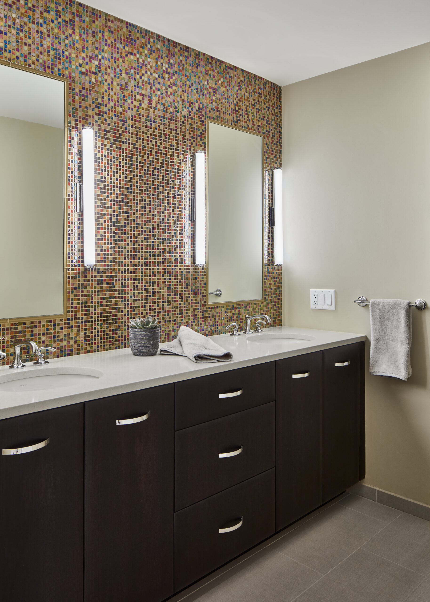 Experience luxury interior design with this double bathroom vanity featuring dark wood cabinets, a white countertop, two mirrors, wall-mounted lights, a colorful mosaic backsplash, and towels—perfect inspiration for any interior designer in Massachusetts.