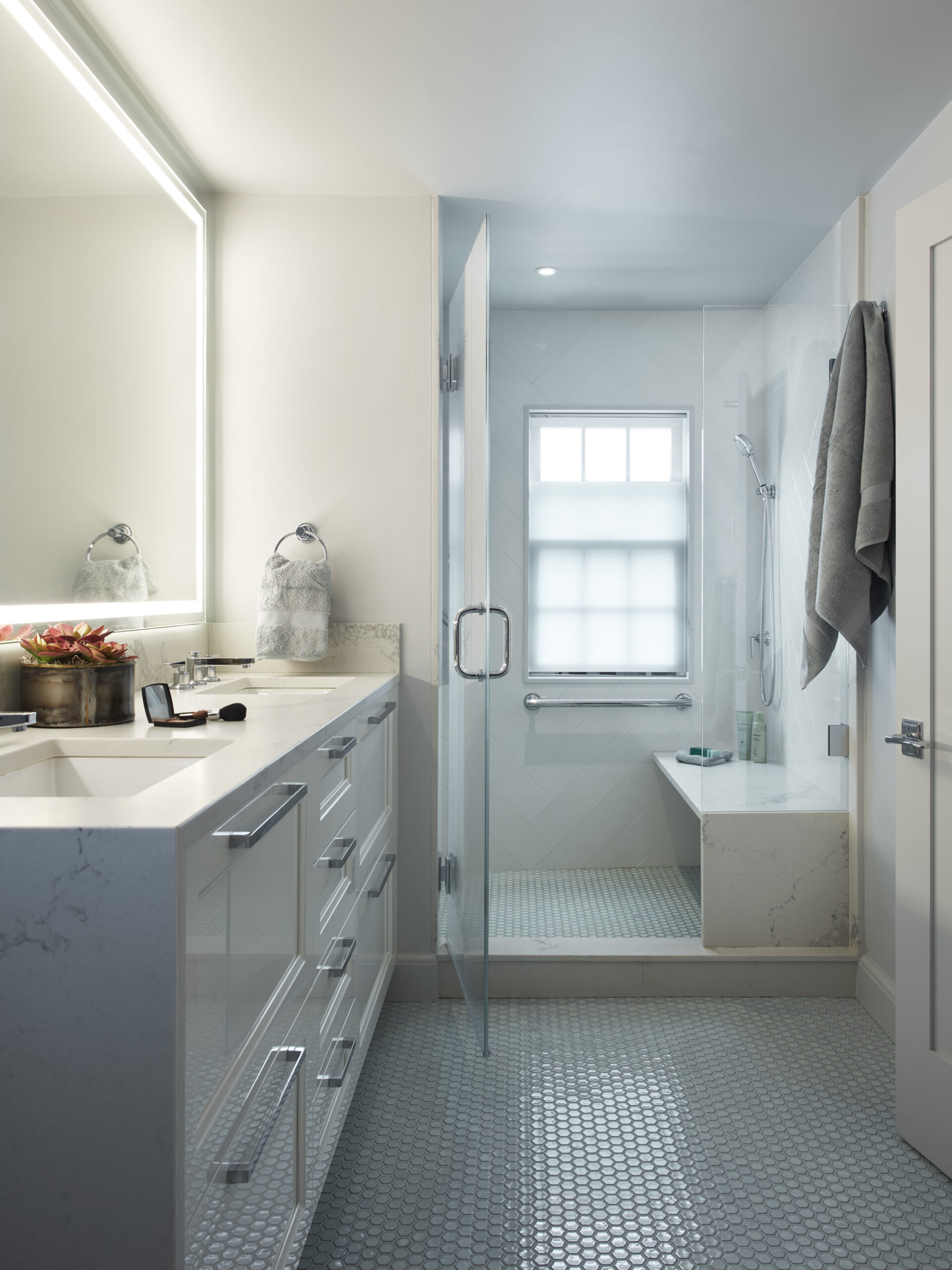 Modern bathroom with white cabinets, a large mirror, glass shower enclosure, towel hanging on the wall, and a window above a bathtub—showcasing Luxury Interior Design crafted by an expert Interior Designer Massachusetts.