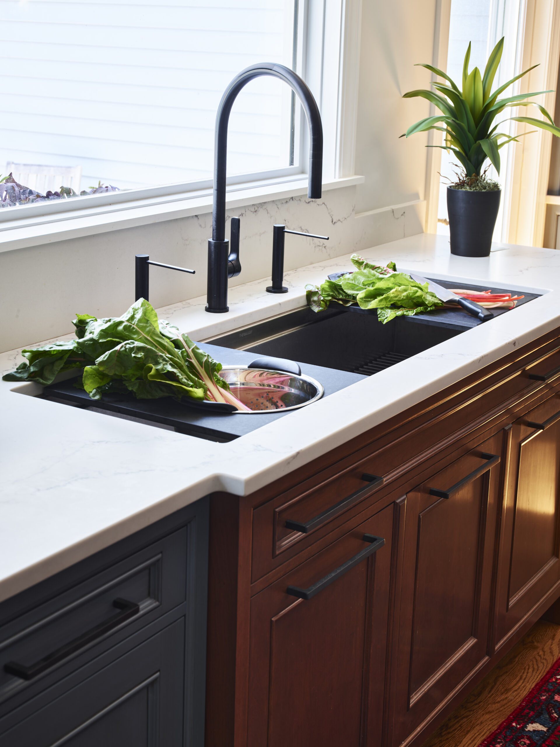 A kitchen sink with leafy greens being washed, a potted plant on the counter, and sunlight streaming in—a touch of Luxury Interior Design for those who appreciate beauty in the everyday.