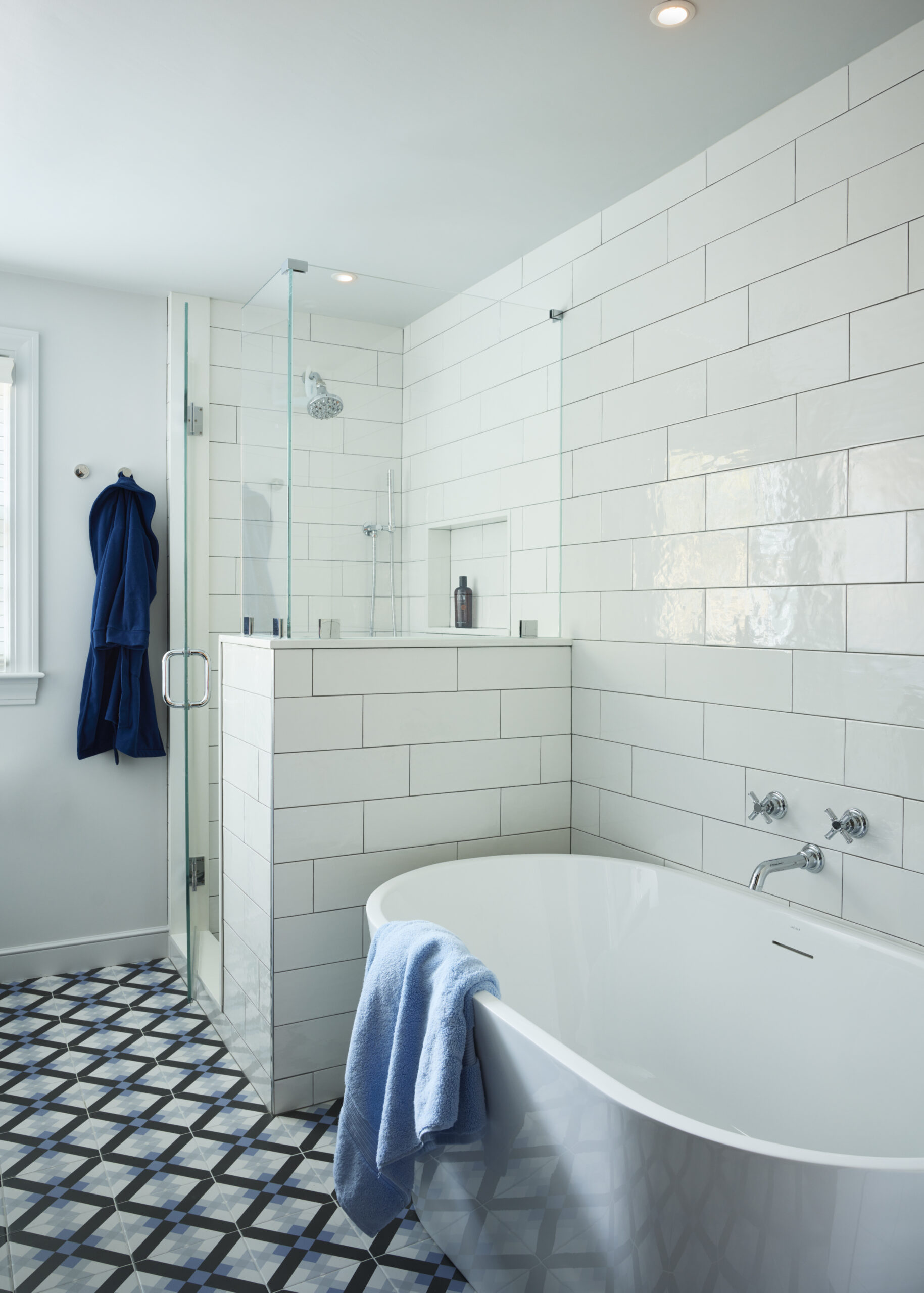 Modern bathroom with white subway tiles, a glass shower enclosure, freestanding tub, geometric patterned floor, and a blue towel draped over the tub—an elegant touch of luxury interior design.