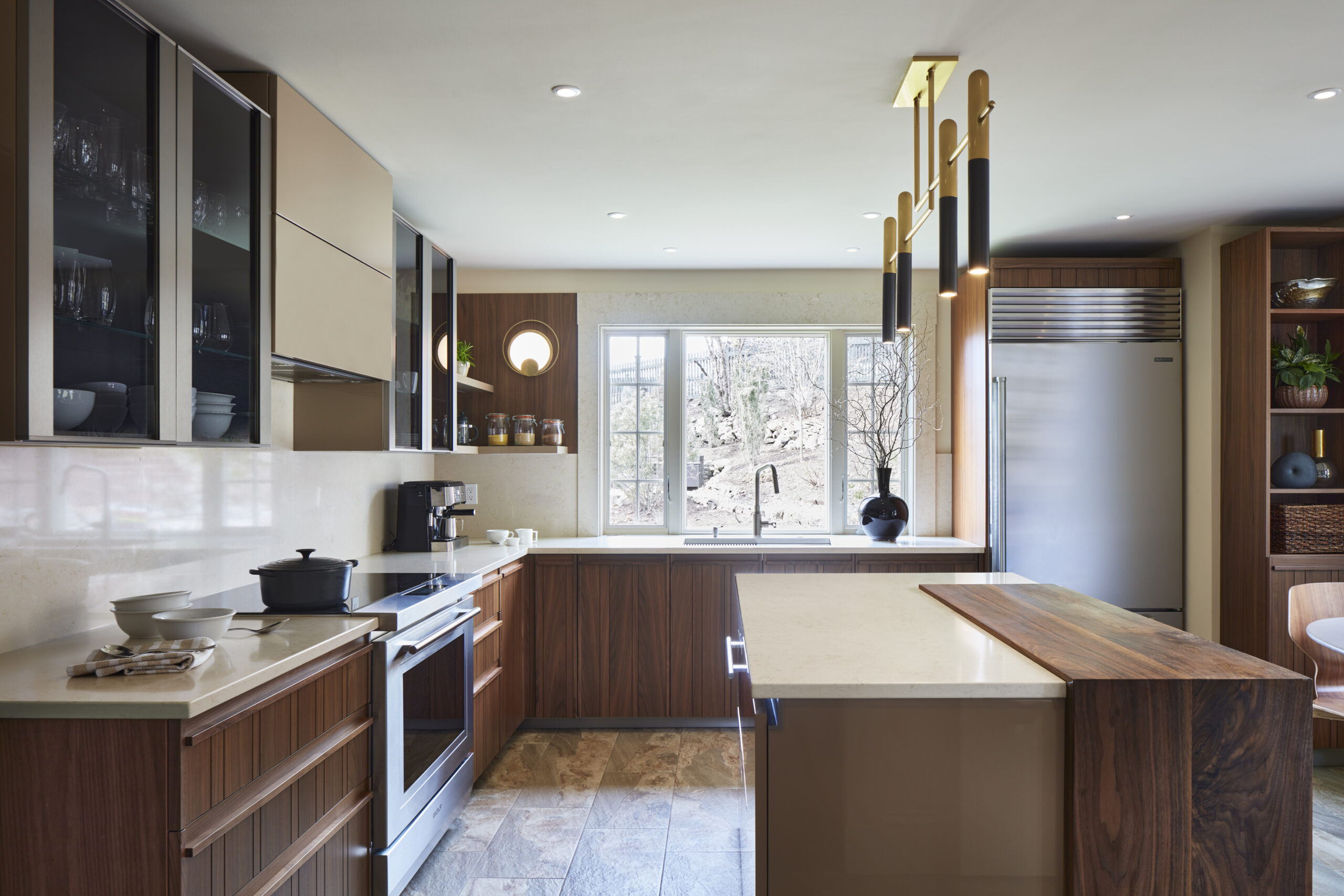 Modern kitchen with wood and beige cabinetry, stainless steel appliances, pendant lights, and a large window above the sink letting in natural light—perfect for those seeking luxury interior design by an expert Interior Designer Massachusetts.