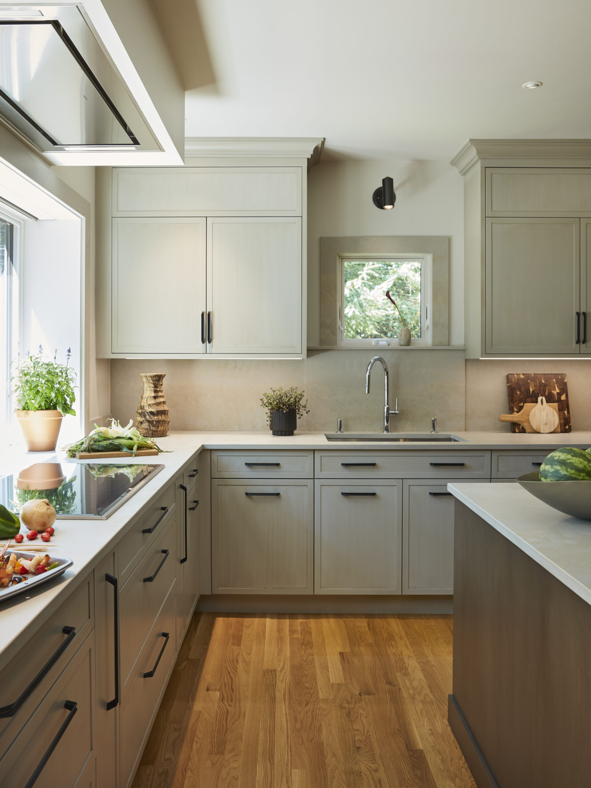 Modern kitchen with light wood cabinets, black handles, wood flooring, a sink under a window, and vegetables on the countertops—showcasing luxury interior design inspired by top interior designers in Massachusetts.