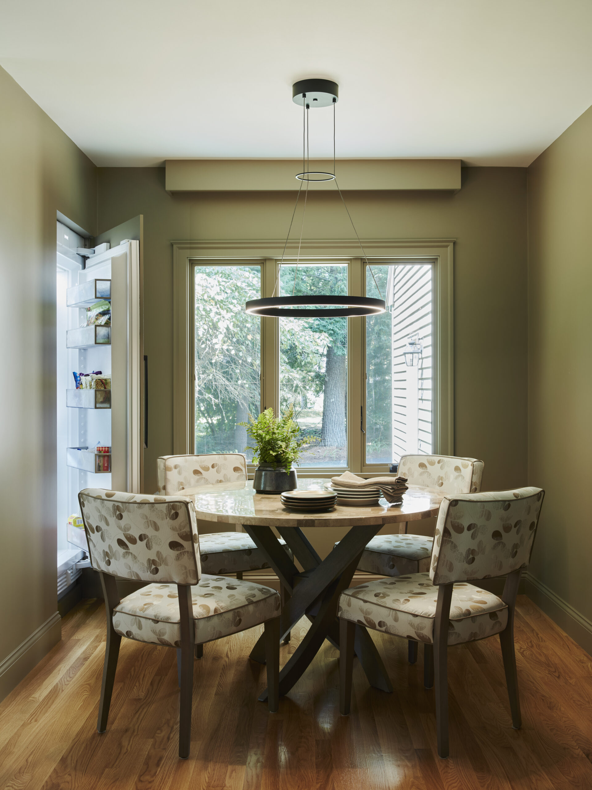 A small dining area with four patterned chairs around a wooden table, set near a large window, and an open refrigerator on the left side—perfect for those seeking luxury interior design with a touch of elegance.