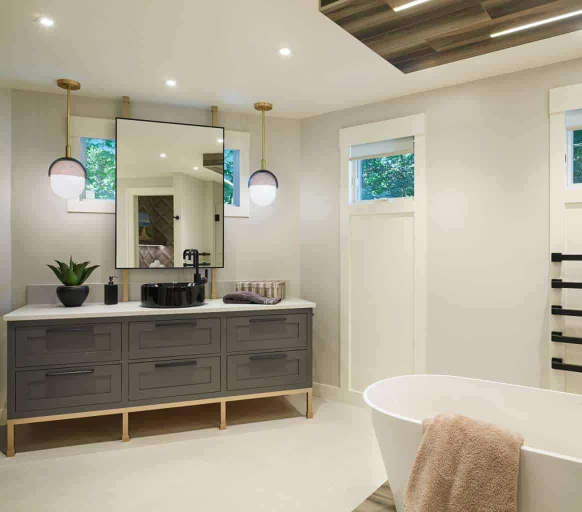 Modern bathroom with a gray vanity, black fixtures, two round pendant lights, a large mirror, and a freestanding tub. Designed by an Interior Designer Massachusetts, this space showcases luxury interior design with abundant natural light.