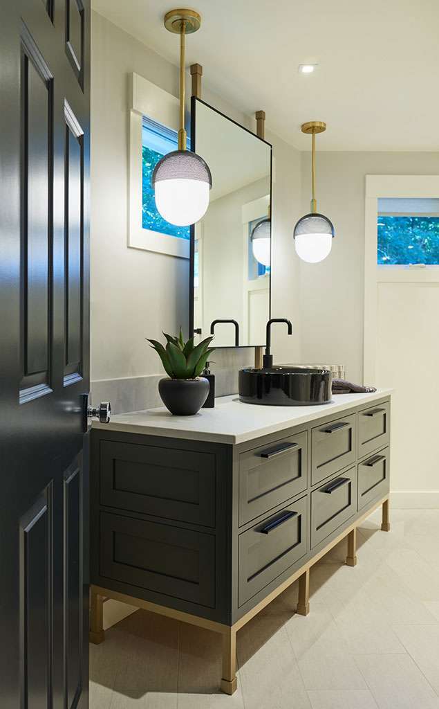 Modern bathroom with a dark double-sink vanity, large mirror, pendant lights, potted plant, and natural light from small windows—showcasing luxury interior design by an expert Interior Designer Massachusetts.