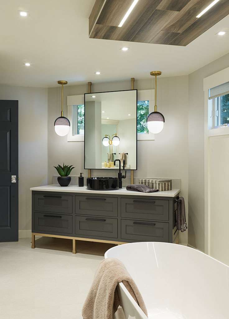 Modern bathroom with a dark gray vanity, black sink, large mirror, stylish pendant lights, potted plant, and a white freestanding bathtub—an exquisite example of Luxury Interior Design by an expert Interior Designer Massachusetts.