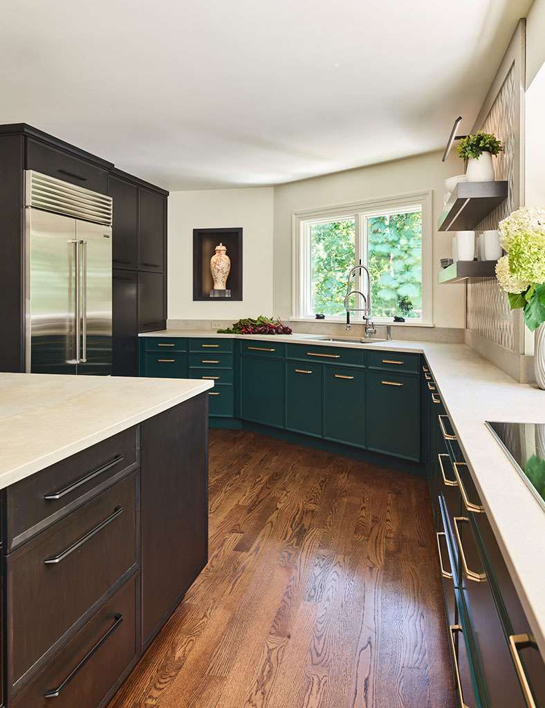 Modern kitchen with dark green and black cabinets, stainless steel appliances, wood floor, large window over the sink, and light-colored countertops—an example of luxury interior design by a top Interior Designer in Massachusetts.