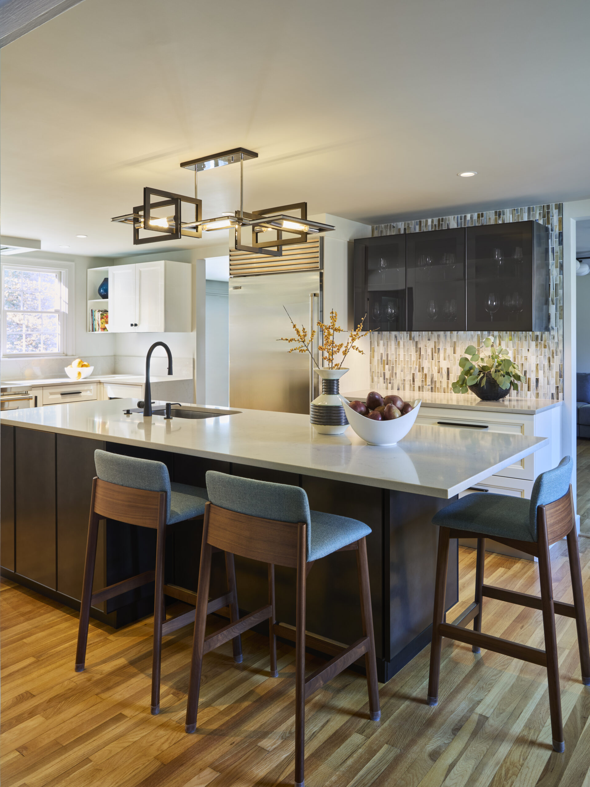 Modern kitchen with a large island, three bar stools, pendant lighting, a bowl of fruit, and contemporary cabinetry on a hardwood floor—perfectly styled for luxury interior design by an expert interior designer in Massachusetts.
