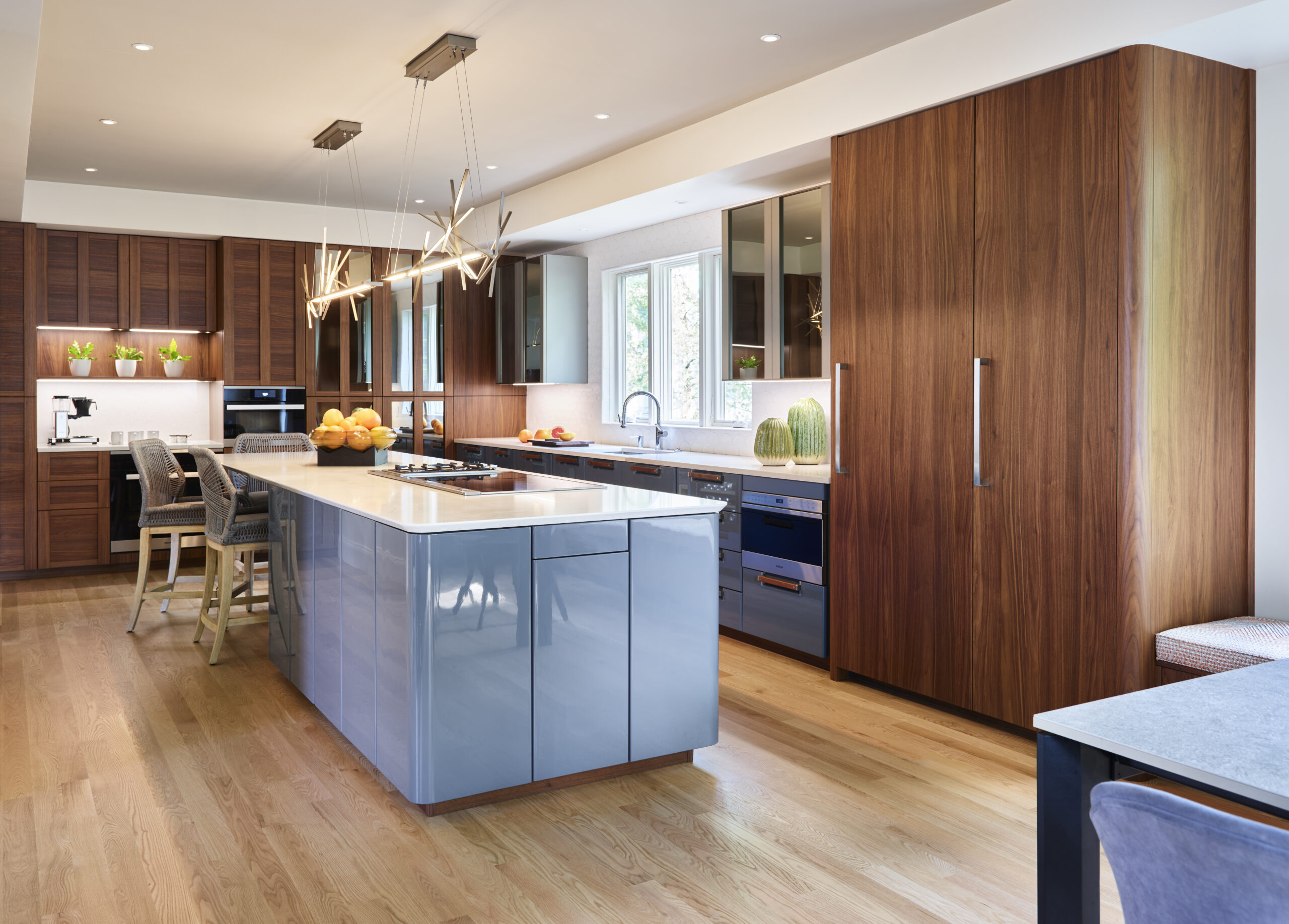 Modern kitchen with wooden cabinets, a blue glossy island, built-in appliances, pendant lights, and large windows over the sink—an example of luxury interior design by a top interior designer in Massachusetts.