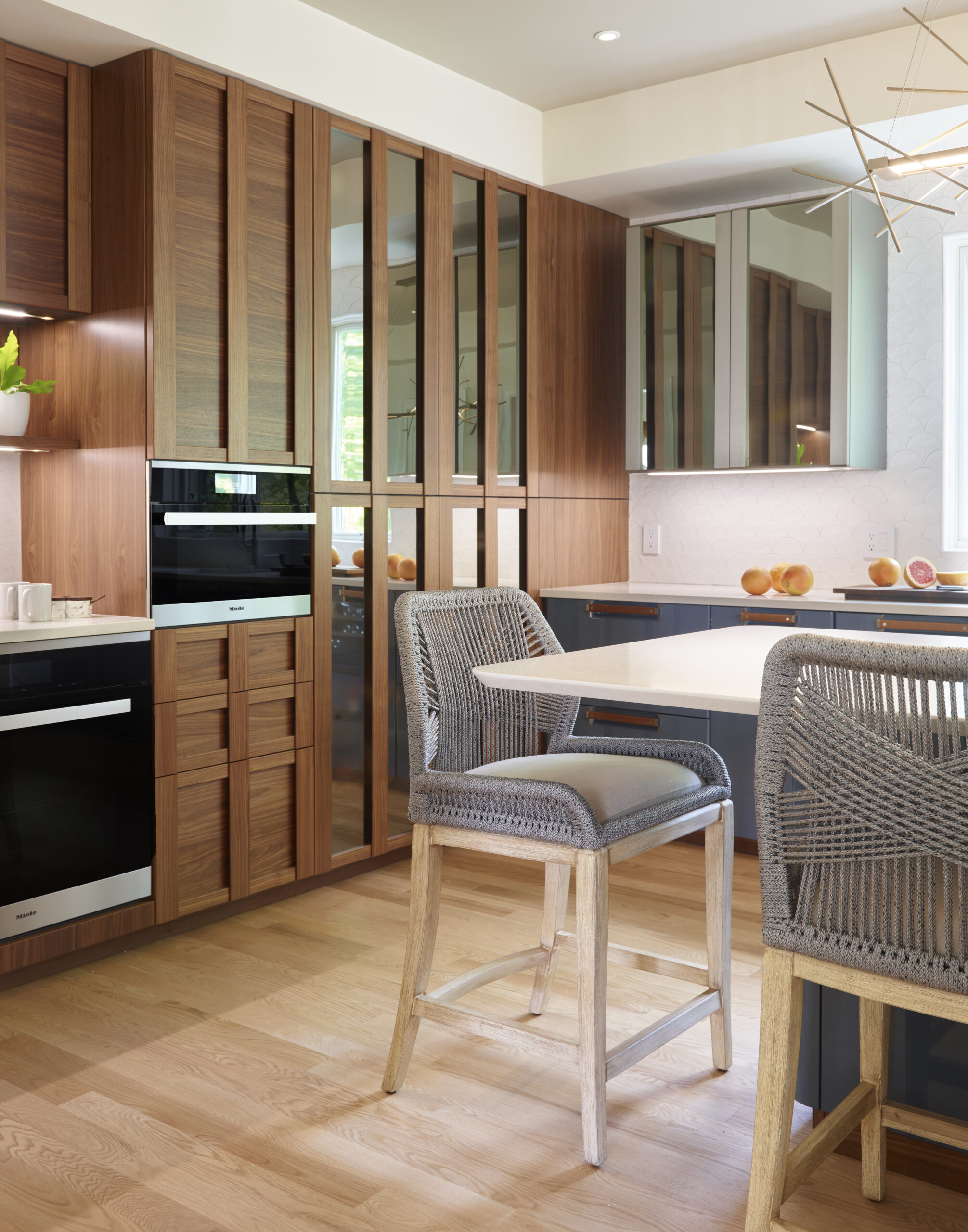 Modern kitchen with wood cabinets, a built-in stainless steel oven, white countertop island, woven bar stools, and ample natural light—a stunning example of luxury interior design by an expert interior designer in Massachusetts.