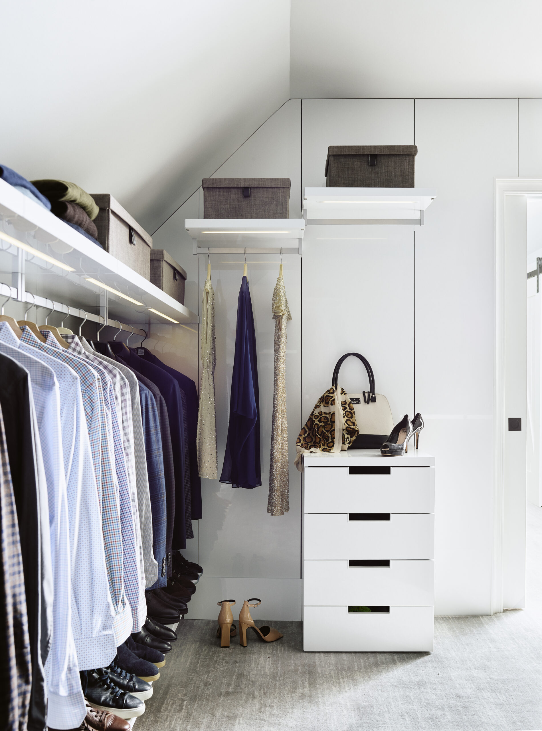A modern walk-in closet designed with Luxury Interior Design in mind, featuring hanging shirts, dresses, storage boxes on shelves, a white drawer unit, handbags, and shoes—all expertly organized for a sophisticated touch.