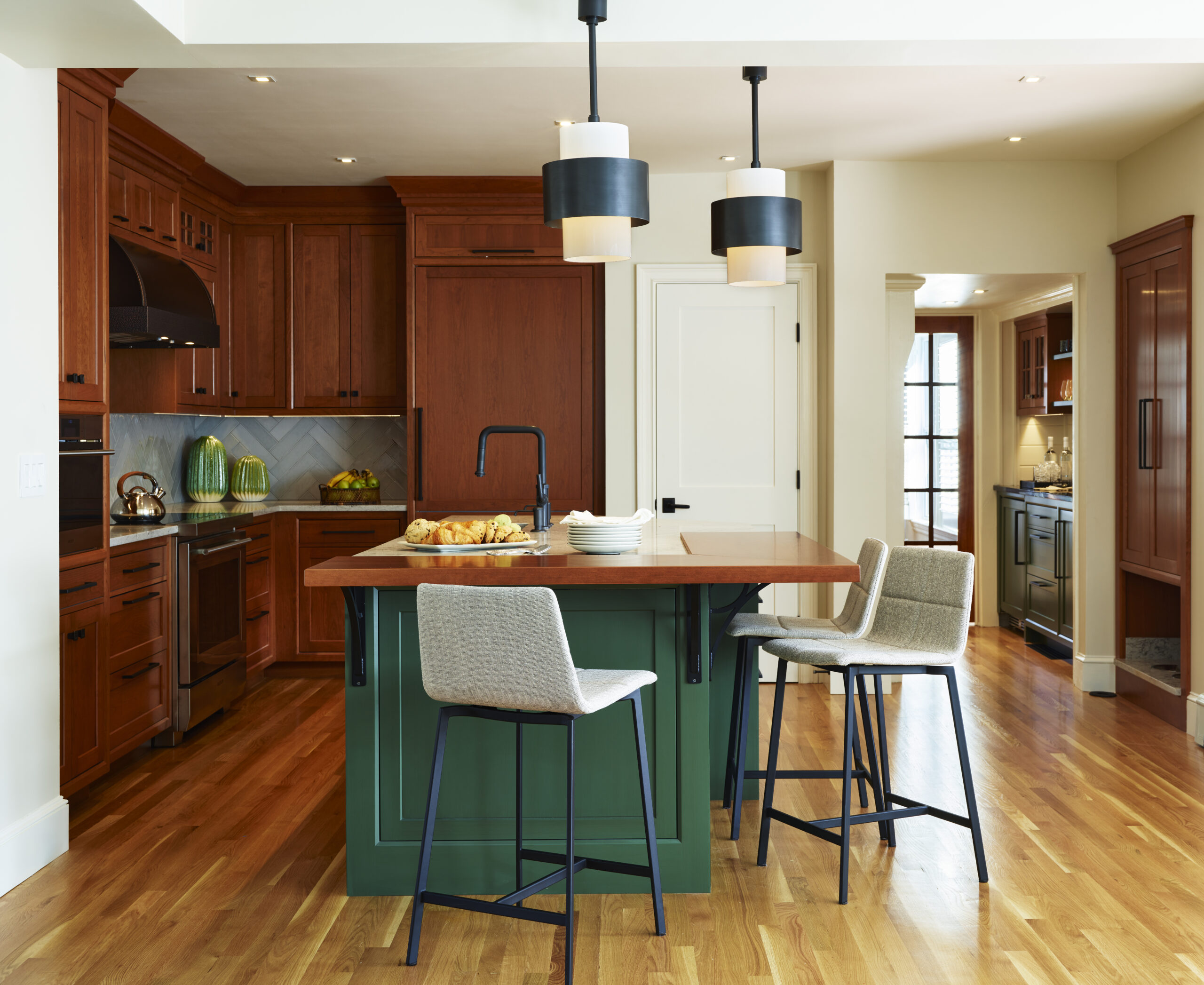 Contemporary kitchen with wooden cabinets, a green island with a wood countertop, modern bar stools, pendant lights, and hardwood floors—an inspiring example of Luxury Interior Design by a top Interior Designer Massachusetts.