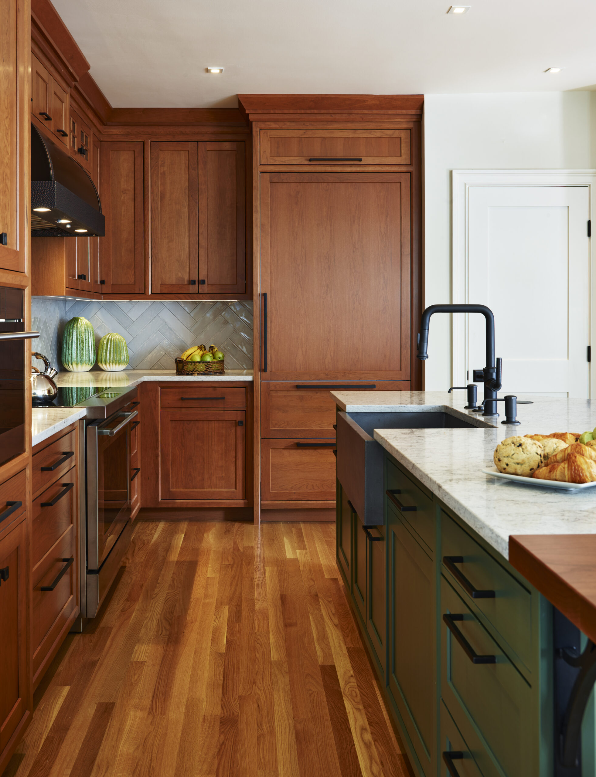 Modern kitchen with wooden cabinets, built-in fridge, stainless steel oven, marble countertop island with black faucet, and hardwood floors. Styled by a top Interior Designer in Massachusetts for a touch of luxury interior design. Bread and pumpkins sit on the island.