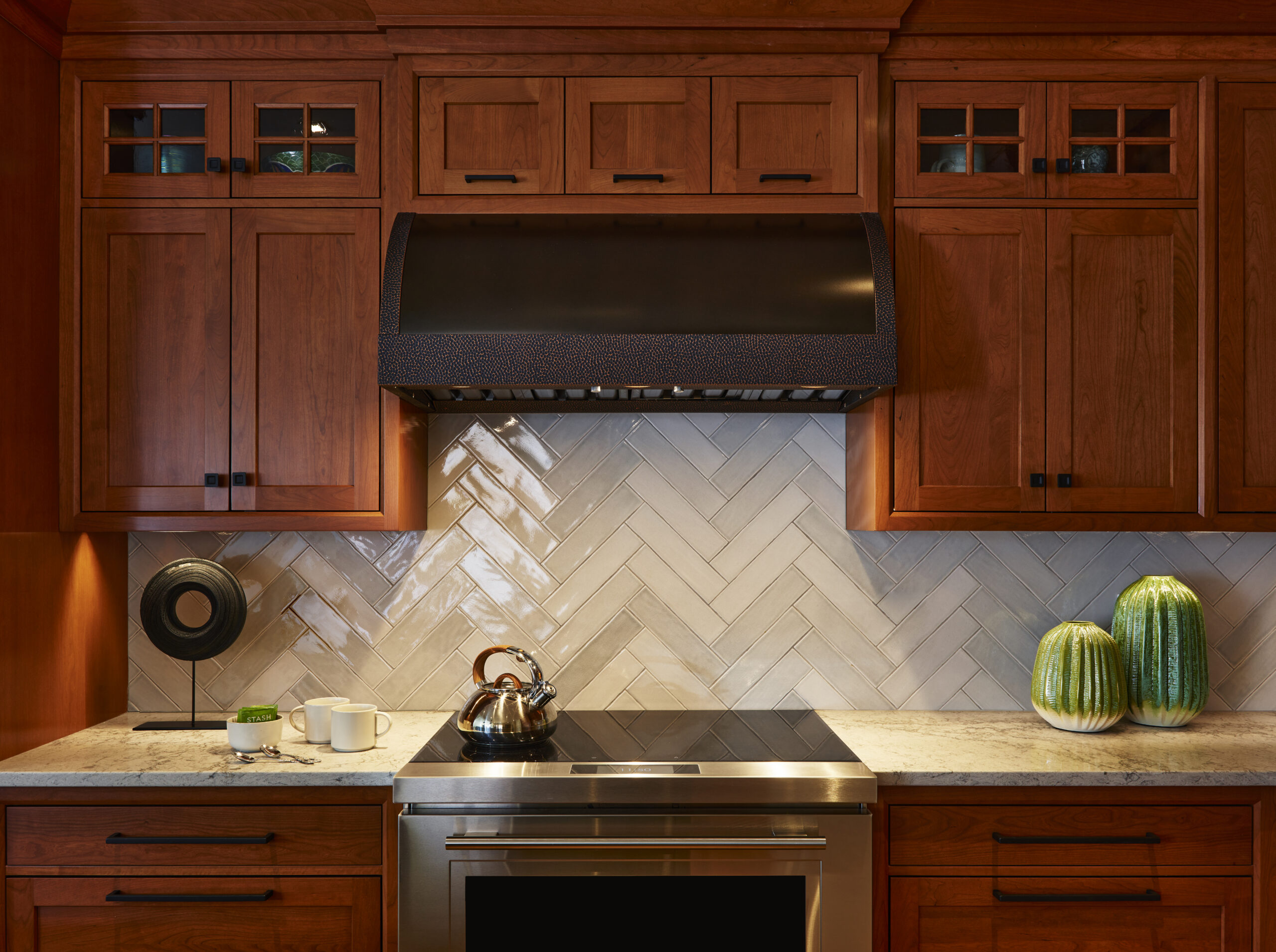 A kitchen designed with wooden cabinets, a black range hood, and luxury interior design details like green decorative vases, reflecting the refined touch of an Interior Designer in Massachusetts.