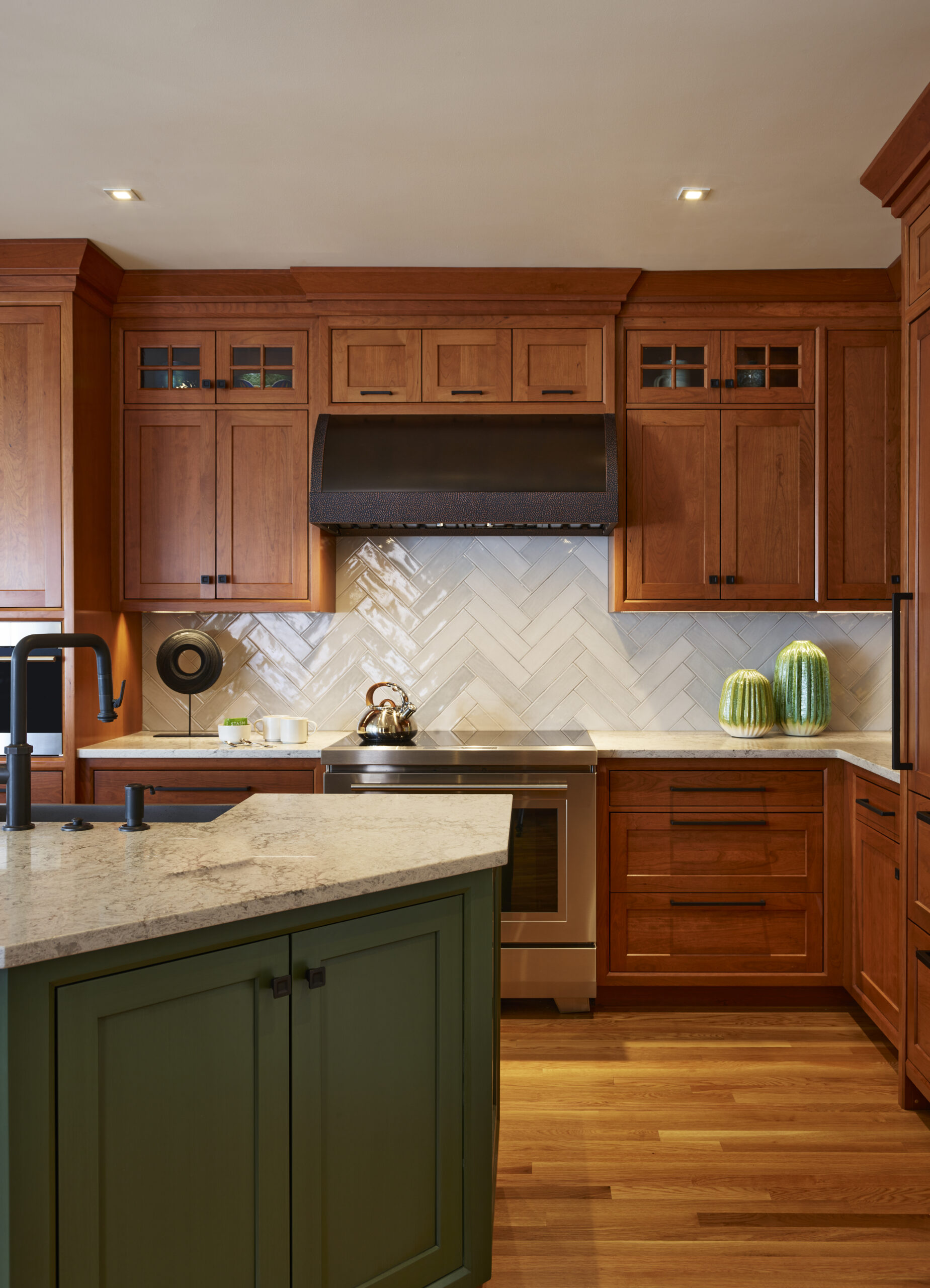 Kitchen with wood cabinets, stainless steel stove, white herringbone tile backsplash, green island, and two green vases on the counter—a beautiful example of luxury interior design.