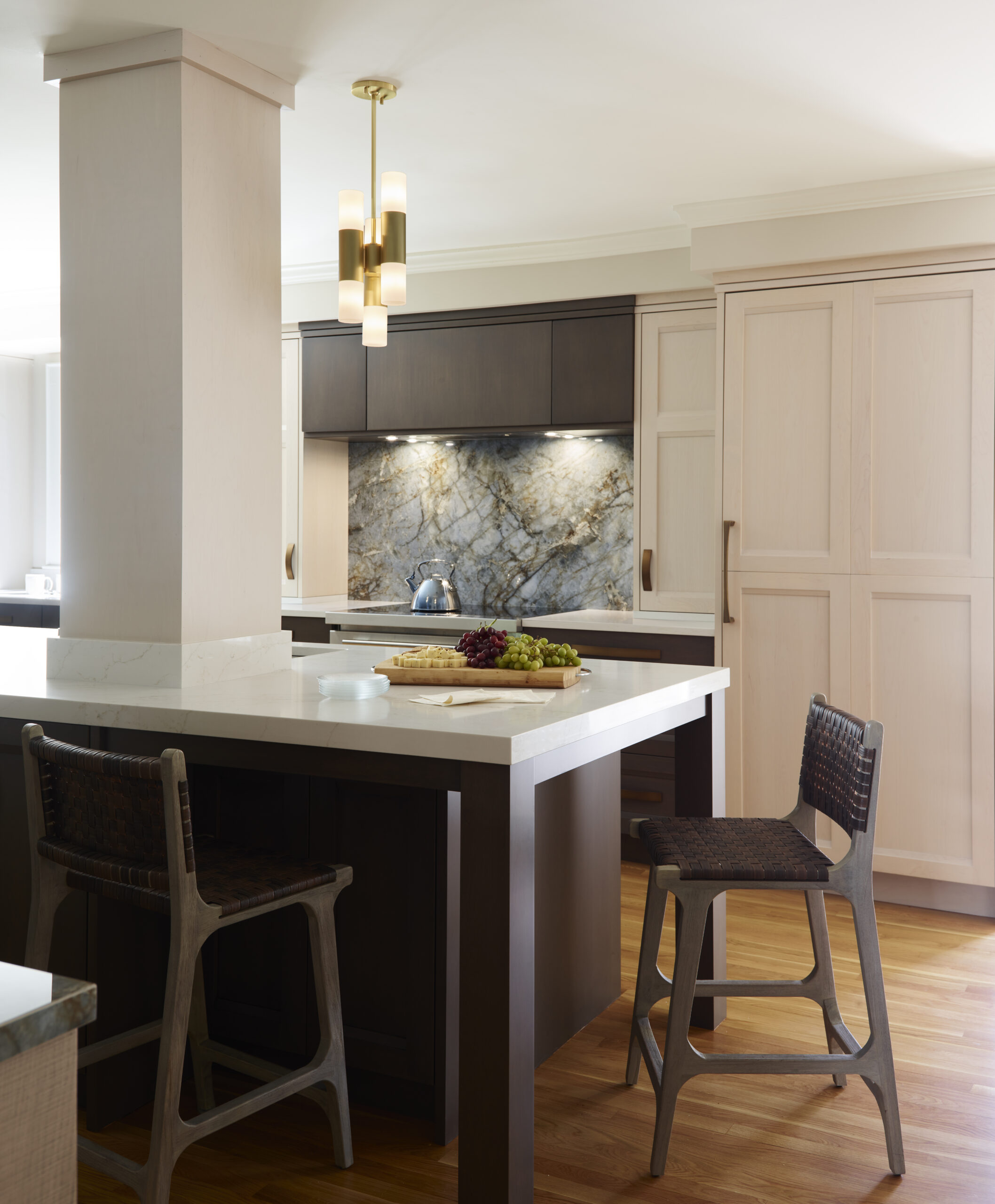 Modern kitchen with light wood cabinets, a marble backsplash, a large center island with two bar stools, and a contemporary pendant light overhead—showcasing luxury interior design by an expert interior designer in Massachusetts.
