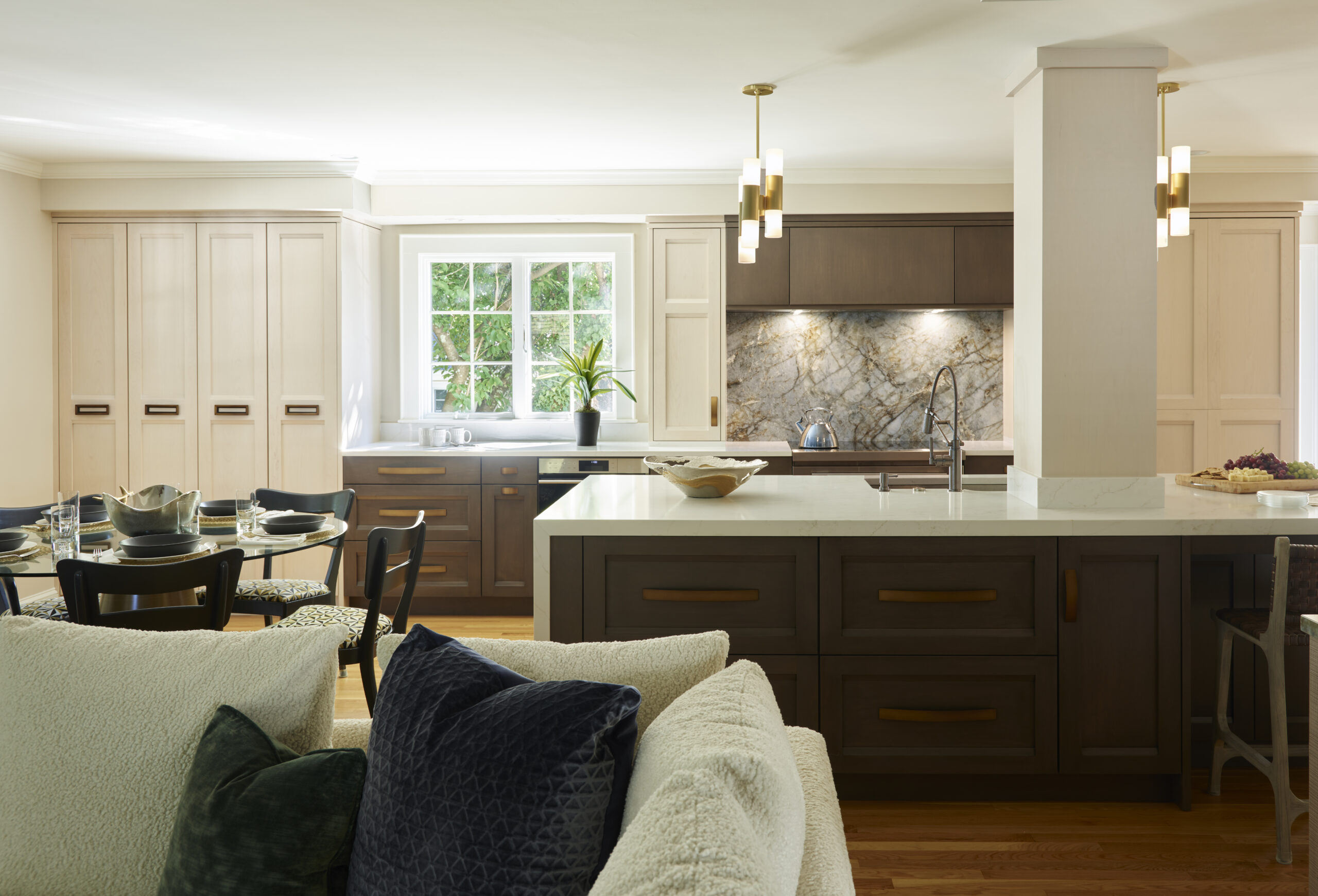 Modern kitchen with a large island, dark wood cabinets, marble backsplash, sink, dining table, and a window letting in natural light—showcasing the elegance of luxury interior design by an experienced interior designer in Massachusetts.