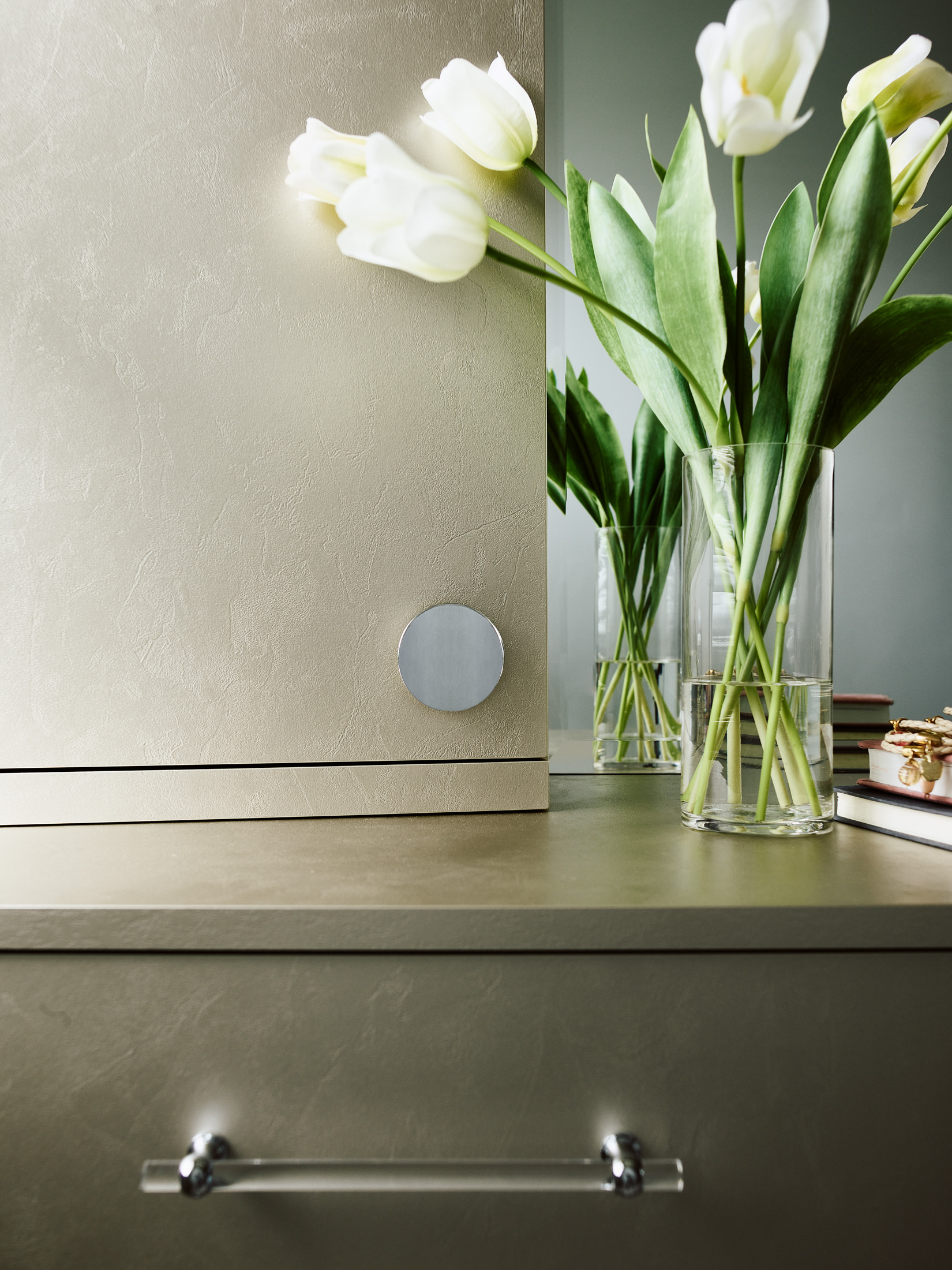 A clear glass vase with white tulips is placed on a beige dresser with a metallic drawer handle and a round silver detail, reflecting the touch of luxury interior design by an expert Interior Designer in Massachusetts.