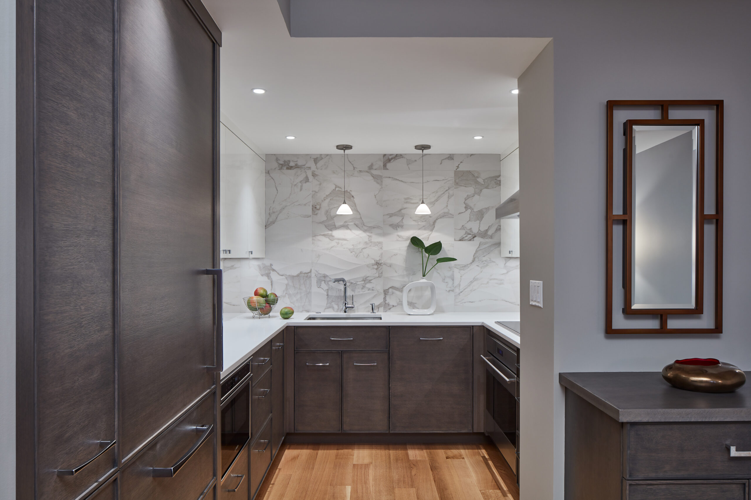 Modern kitchen with dark wood cabinets, white countertops, marble backsplash, and pendant lights. Styled by a top Interior Designer Massachusetts, this space features luxury interior design details like fruit bowls and a vase with greenery.