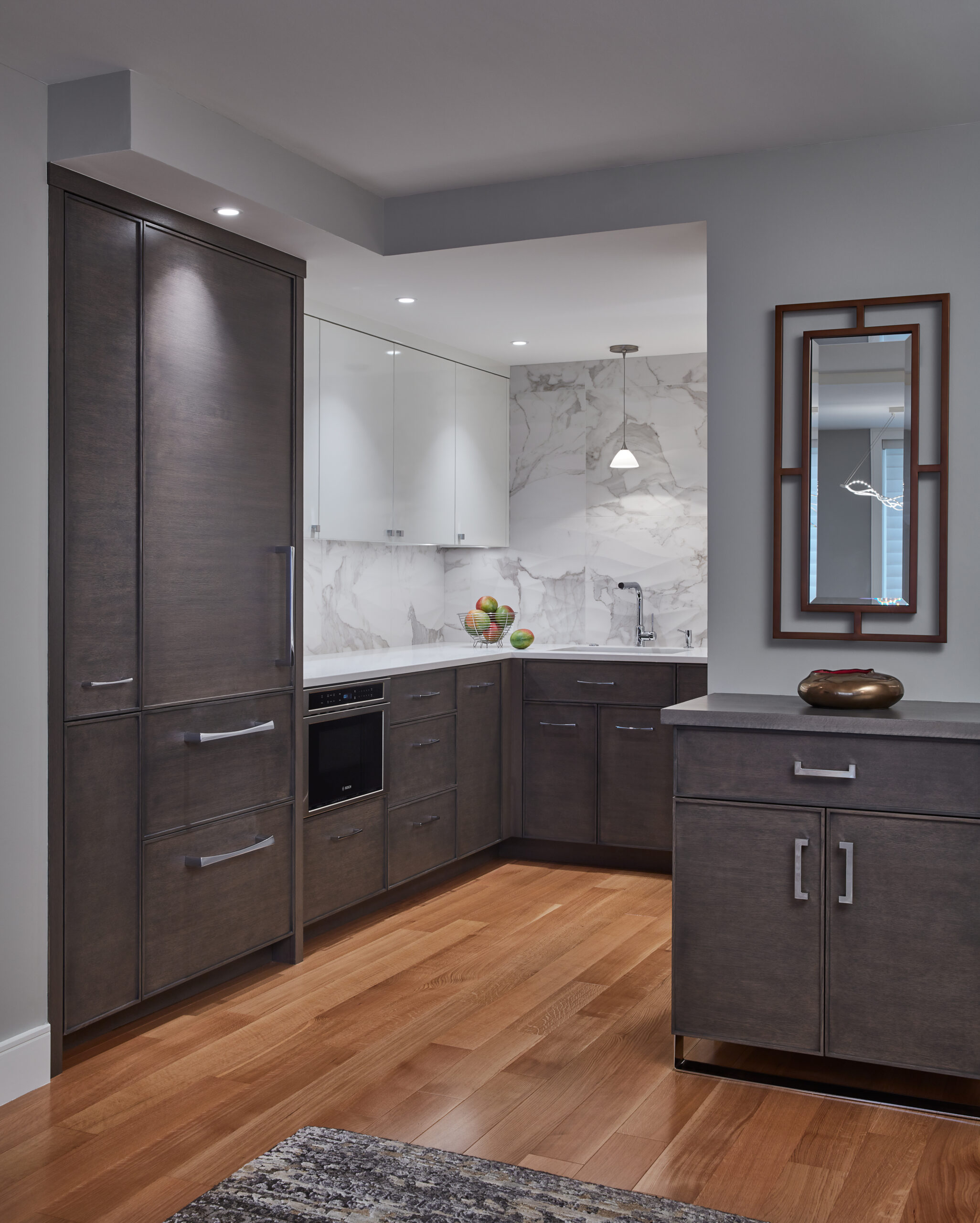 Modern kitchen with dark wood cabinets, white marble backsplash, stainless steel hardware, light wood floor, and a countertop with a fruit bowl under pendant lighting—showcasing the elegance of luxury interior design.