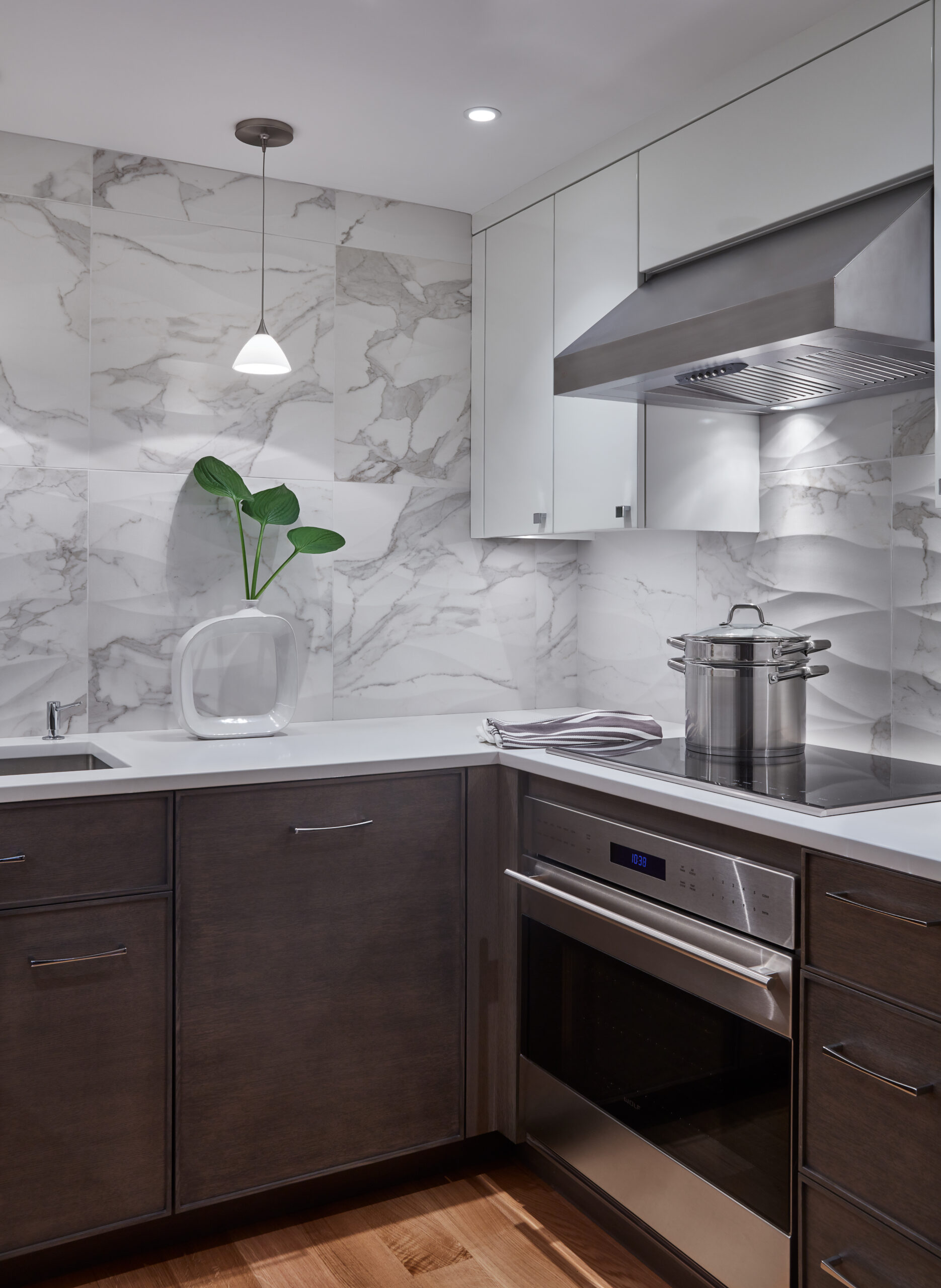 Modern kitchen with dark cabinets, white countertops, marble backsplash, stainless steel appliances, and a white vase with green leaves—showcasing the sophistication of luxury interior design by an interior designer in Massachusetts.