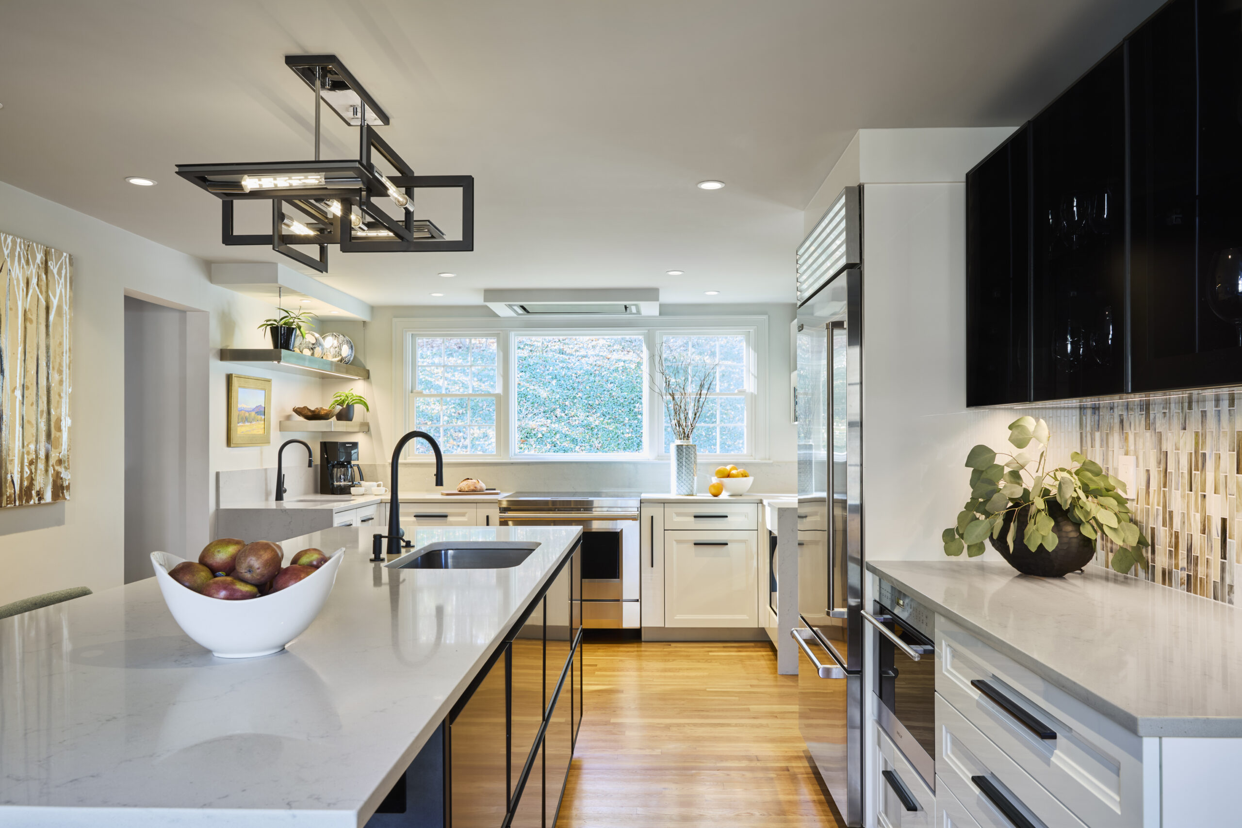 Modern kitchen with white countertops, stainless steel appliances, black cabinets, a bowl of apples on the island, and large windows letting in natural light—an inspiring example of luxury interior design by an Interior Designer Massachusetts.