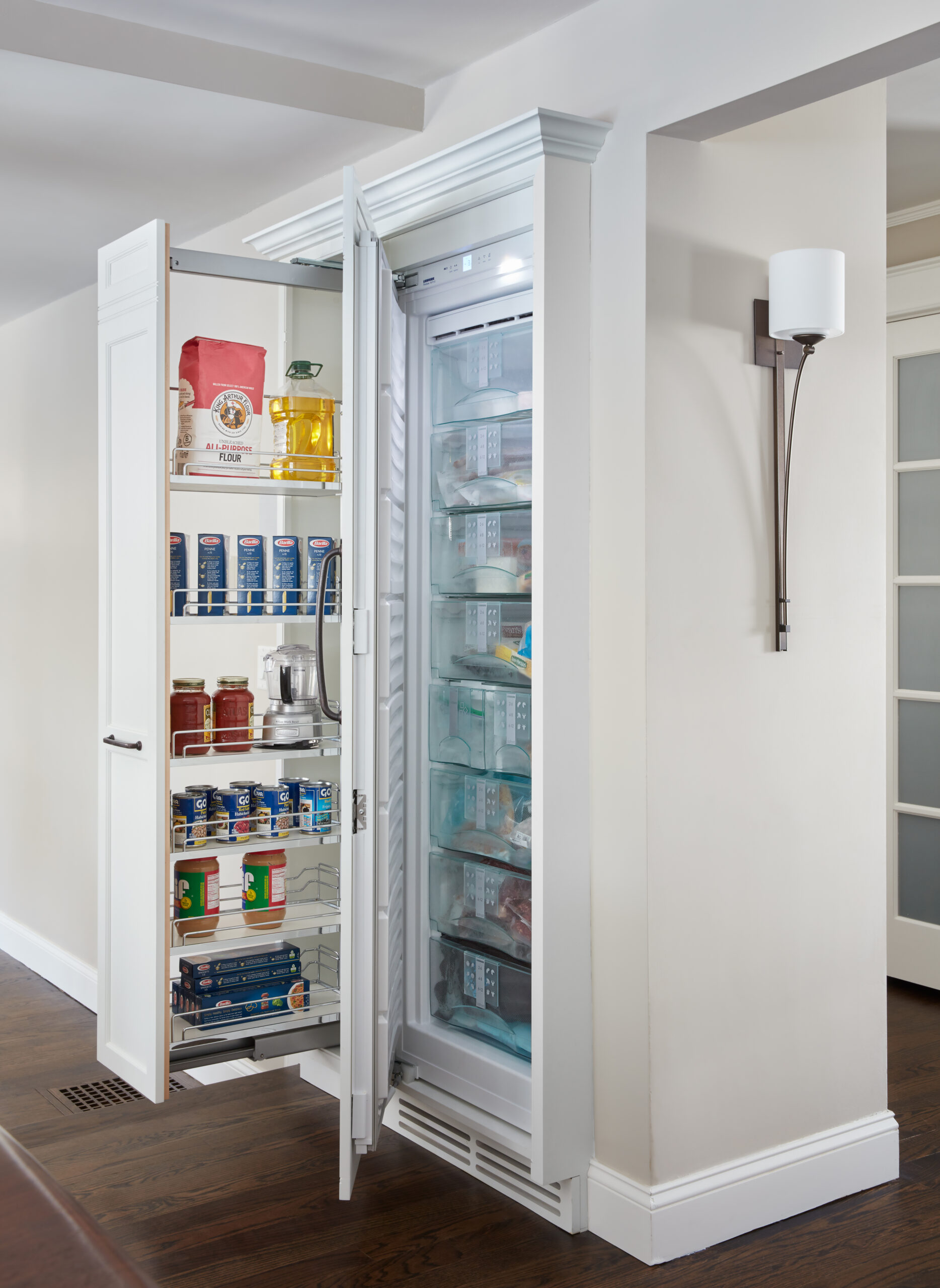 A built-in refrigerator with open doors reveals shelves stocked with groceries, canned goods, beverages, and frozen foods—perfect for a kitchen crafted by a luxury interior design expert or an interior designer in Massachusetts.