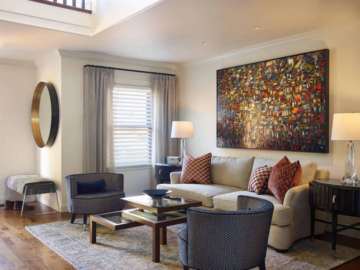 Modern living room with a beige sofa, two patterned armchairs, a glass coffee table, large abstract wall art, a round mirror, and soft lighting—showcasing refined Luxury Interior Design.