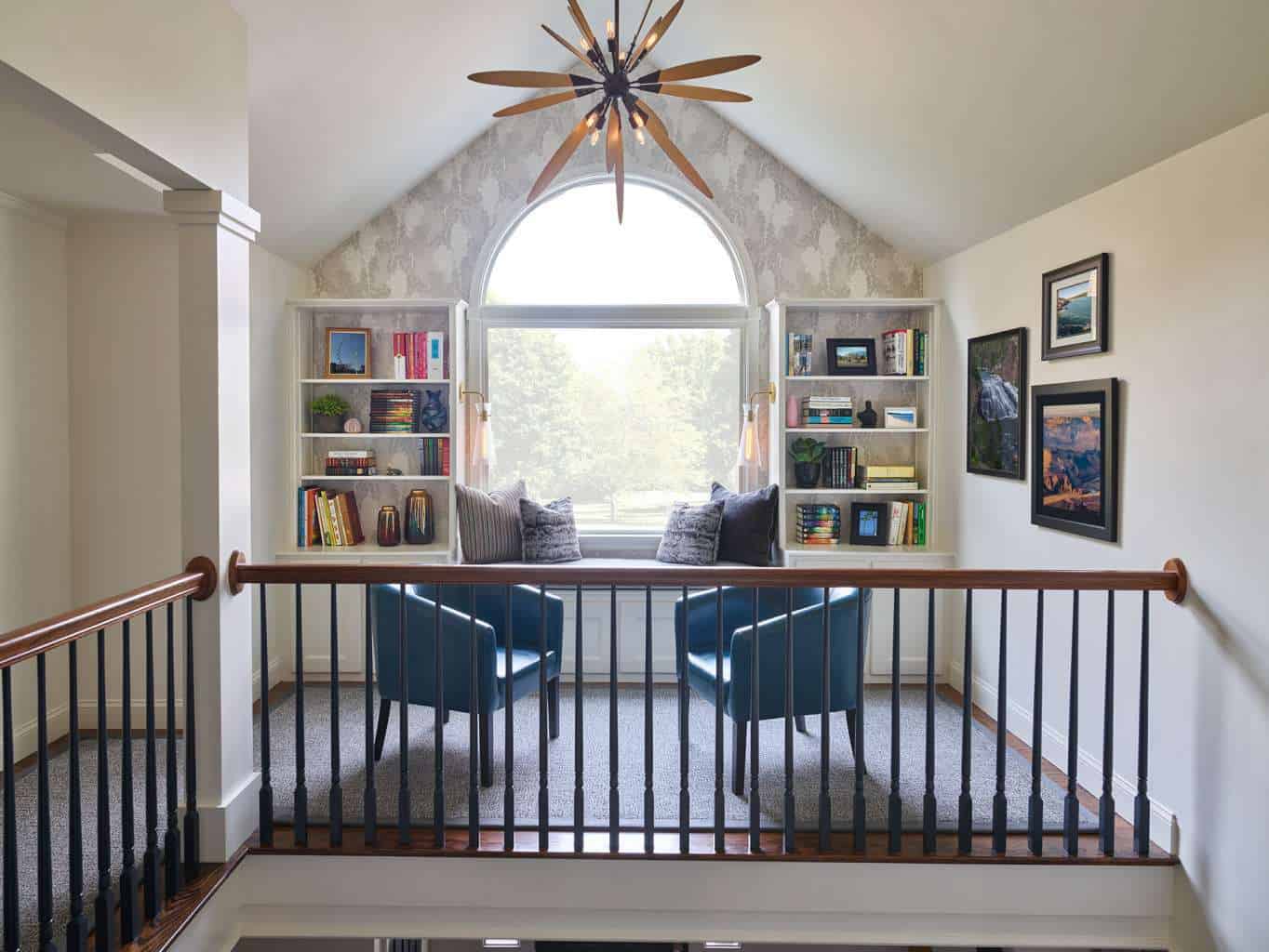 A cozy reading nook with a large arched window, built-in bookshelves, two blue chairs, a window seat with pillows, and a modern chandelier overhead—perfectly showcasing luxury interior design by an expert interior designer in Massachusetts.
