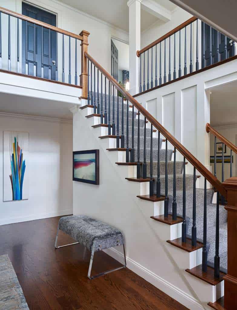 A carpeted staircase with wooden steps and black railings in a modern home showcases luxury interior design, highlighted by artwork on the walls and a cushioned bench near the stairs.