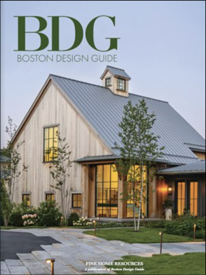 Cover of Boston Design Guide magazine featuring a modern barn-style home with wood siding, metal roof, large windows, and landscaped yard at dusk—showcasing luxury interior design by a top interior designer in Massachusetts.