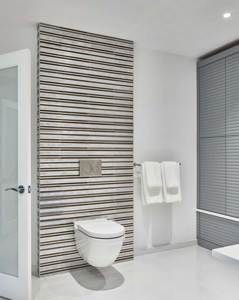 Modern bathroom with a wall-mounted toilet, striped tile accent wall, two folded white towels on a rack, and minimalistic decor—a perfect example of Luxury Interior Design by an expert Interior Designer in Massachusetts.