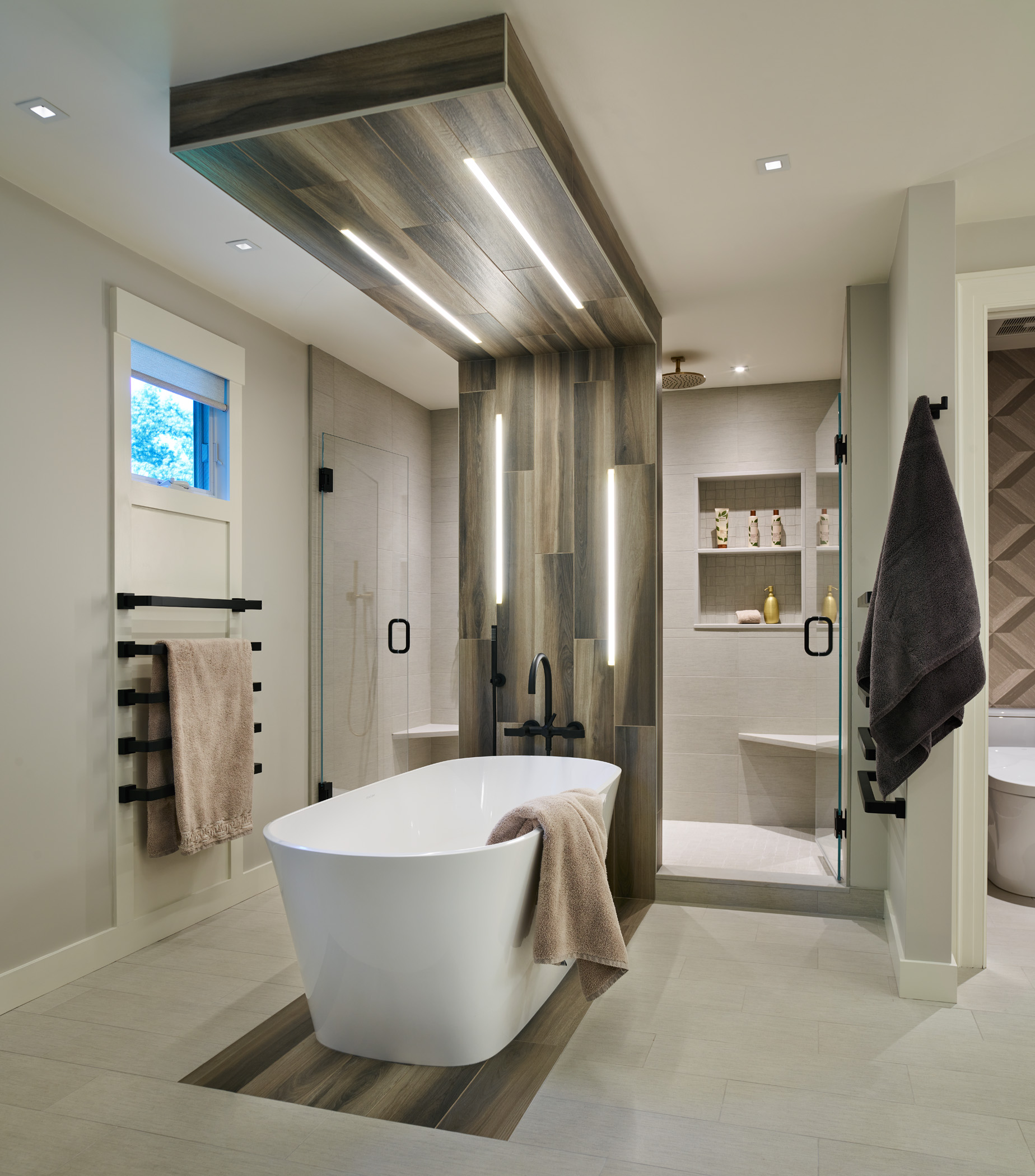 Modern bathroom with freestanding tub, wood accents, walk-in shower, and neutral decor. Designed by an Interior Designer Massachusetts, it features towel racks and built-in wall shelves for a touch of luxury interior design.