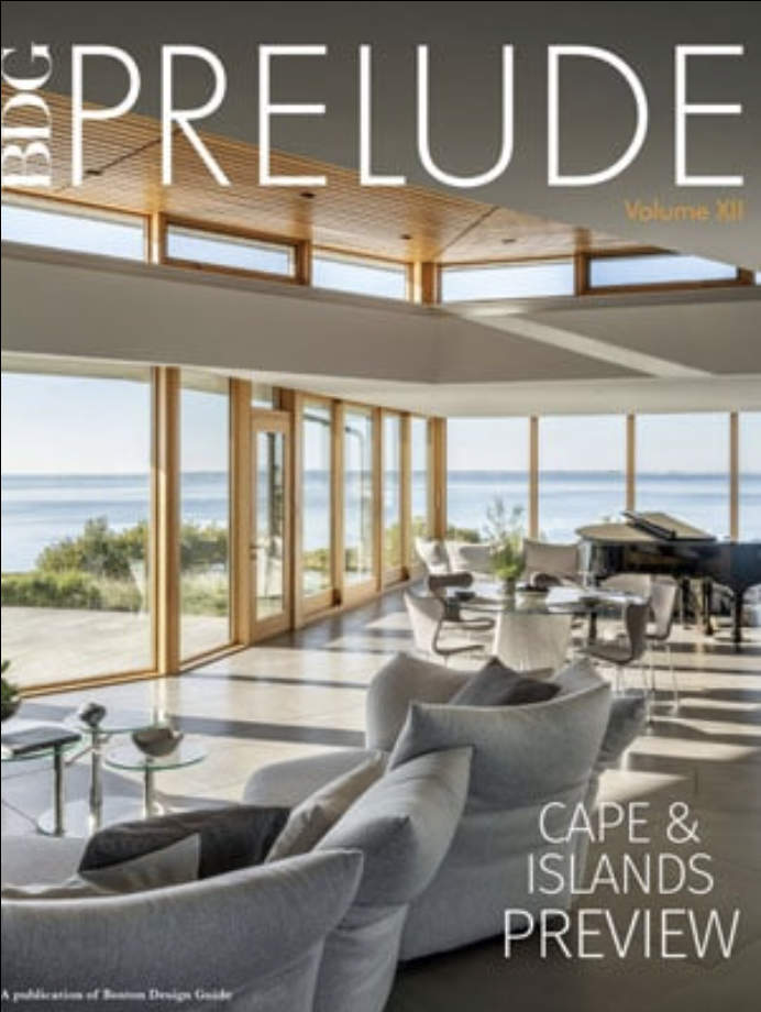 Modern living room with large windows overlooking the ocean, featuring light-colored furniture and a grand piano, showcasing Luxury Interior Design on the cover of BDG Prelude magazine.