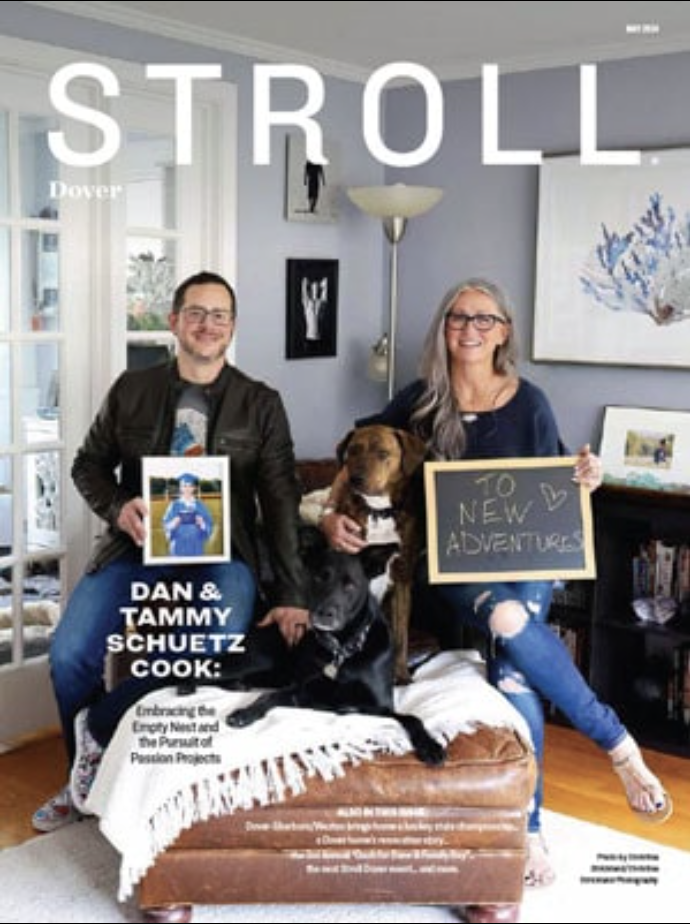 Two people sit with two dogs in a luxury interior design living room. One holds a photo, the other a chalkboard reading 