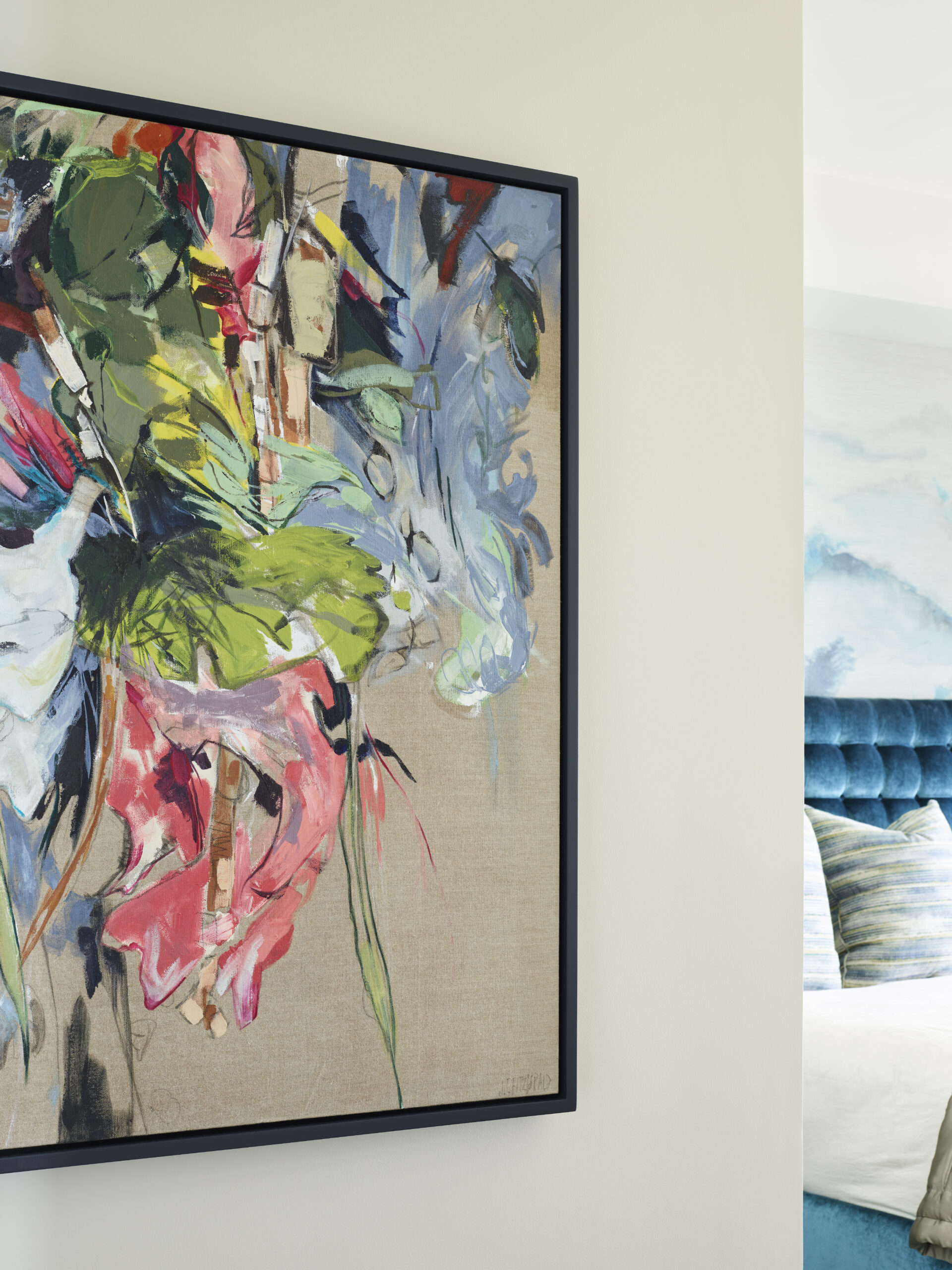 A colorful abstract painting with bold brushstrokes in green, pink, blue, and white hangs on a light wall near a modern, blue-upholstered bed—perfect inspiration for luxury interior design by an Interior Designer Massachusetts.