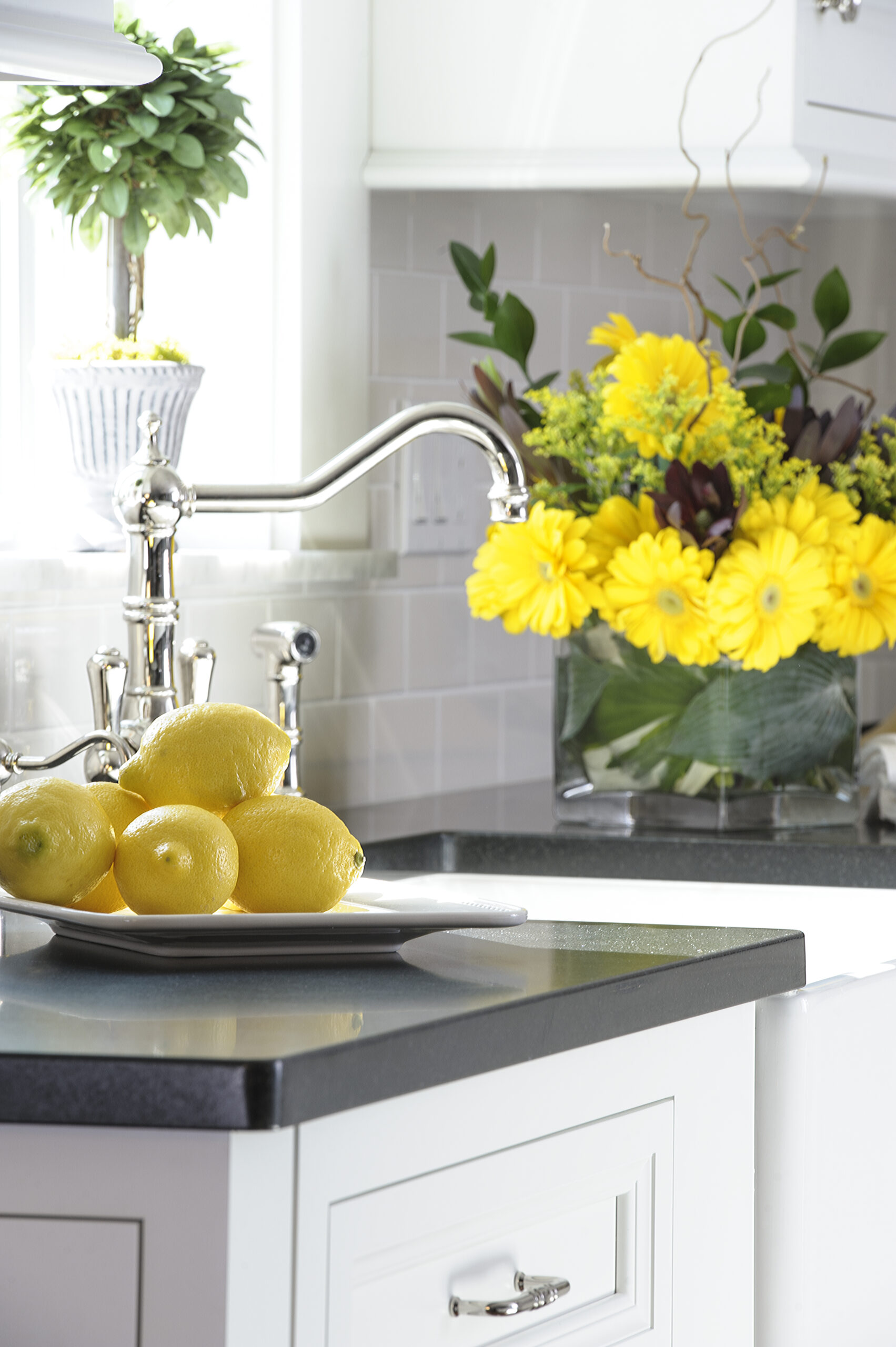 A modern kitchen sink with a chrome faucet, a plate of lemons on the counter, and a vase of yellow flowers near the window reflects the elegance of luxury interior design.