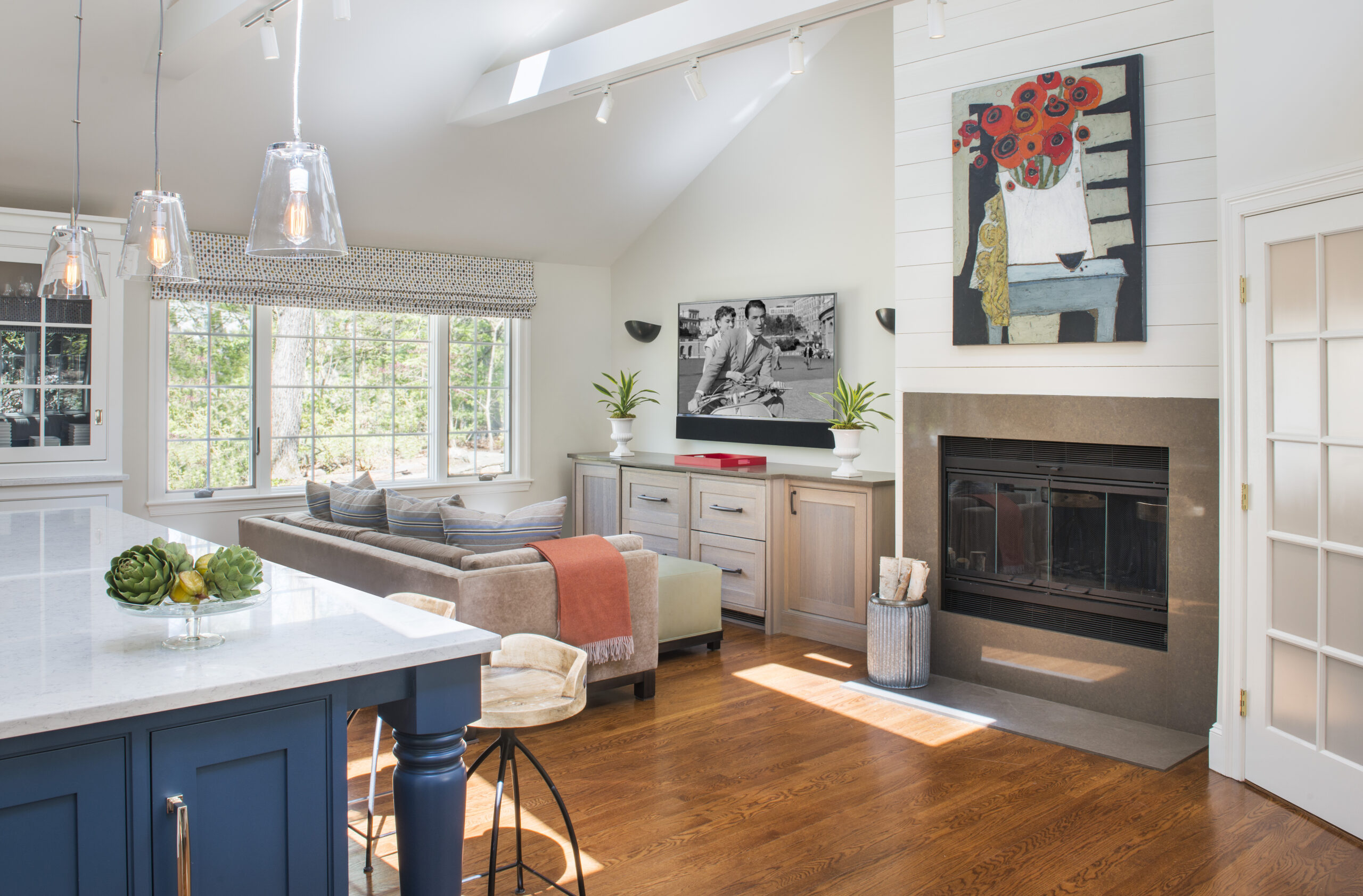 Bright living room with a sofa, TV, fireplace, contemporary decor, large windows, and a kitchen island with stools in the foreground—perfectly styled by a top Interior Designer Massachusetts for luxury interior design enthusiasts.